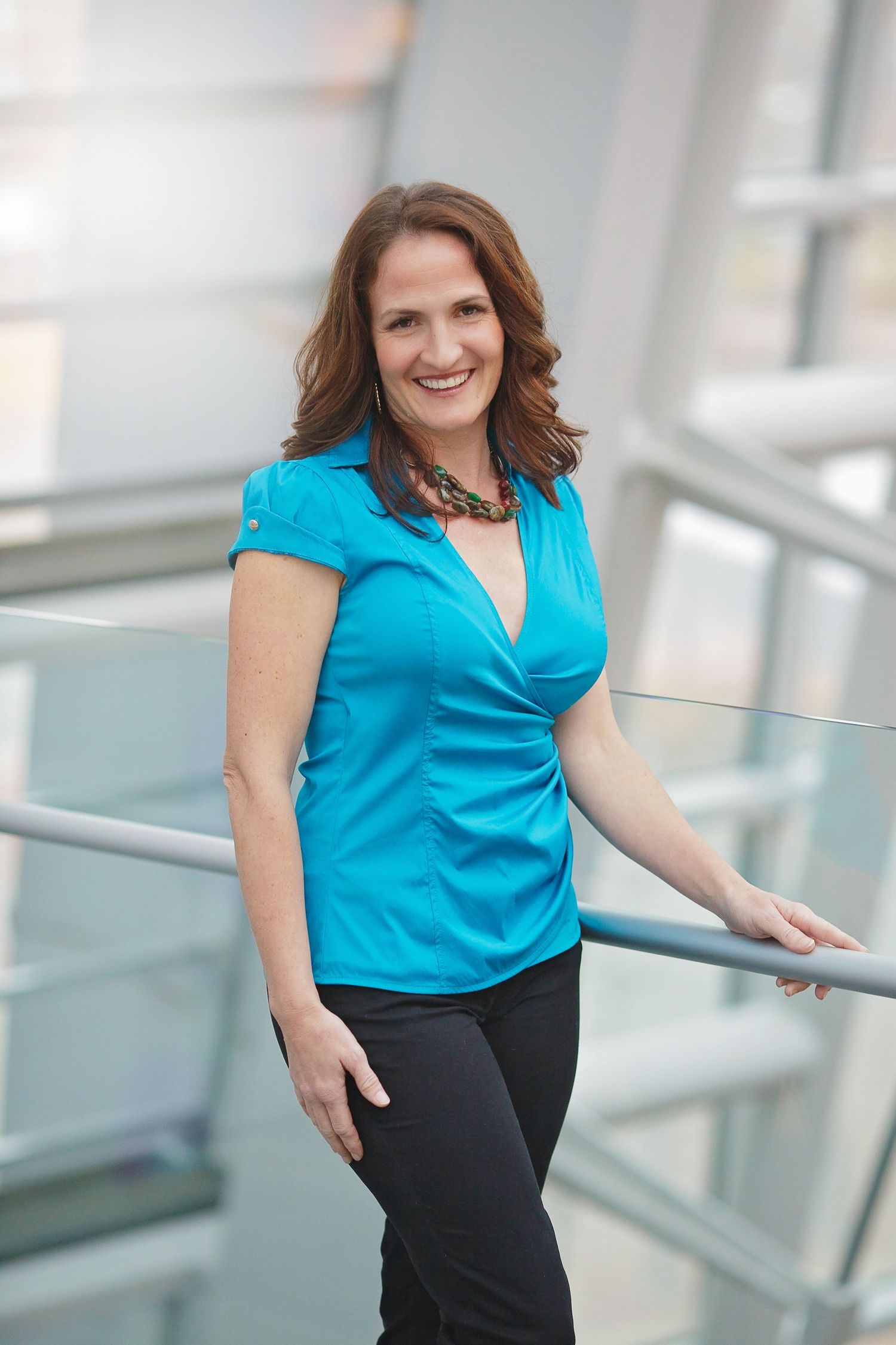 Professional portrait in bright turquoise top against modern office setting.