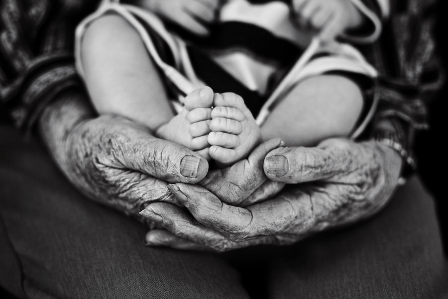 Black and white image of elderly wrinkled hands gently holding tiny baby feet.