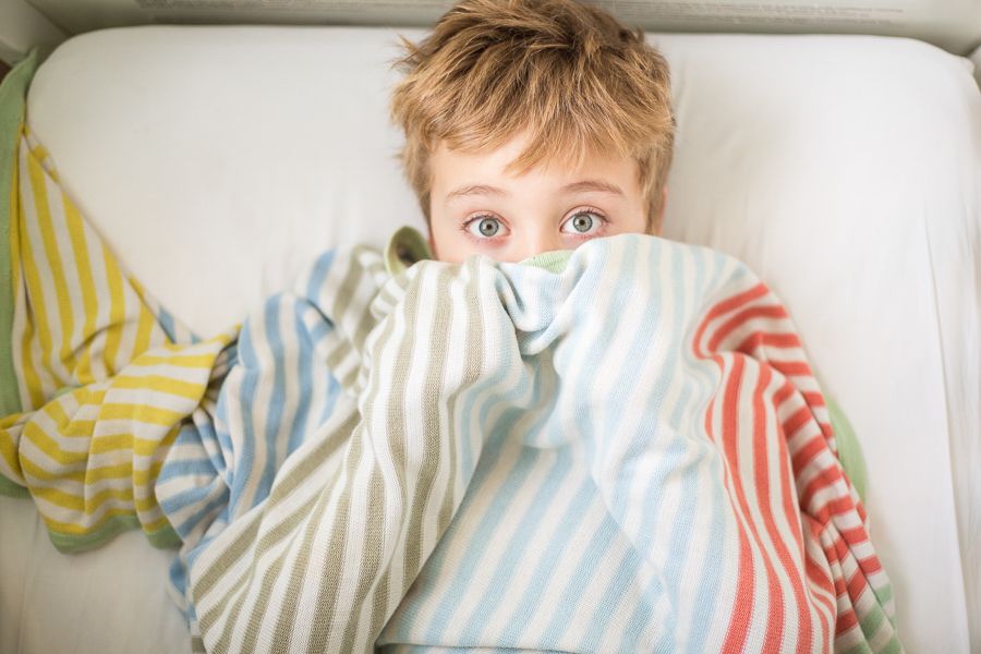 Child peeking out from under striped bedding while laying in bed.