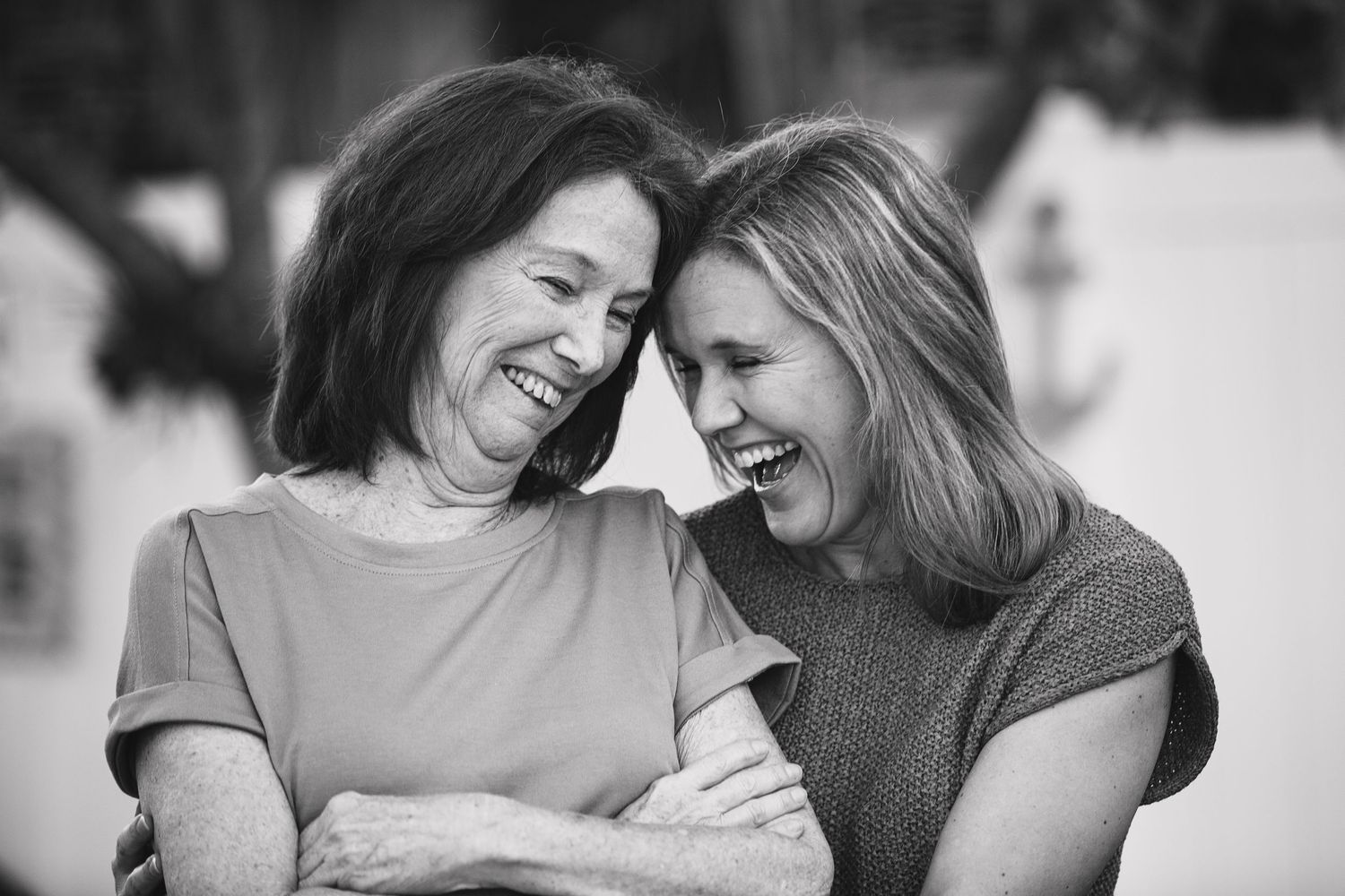 A black and white portrait captures two women sharing a joyful laugh together.