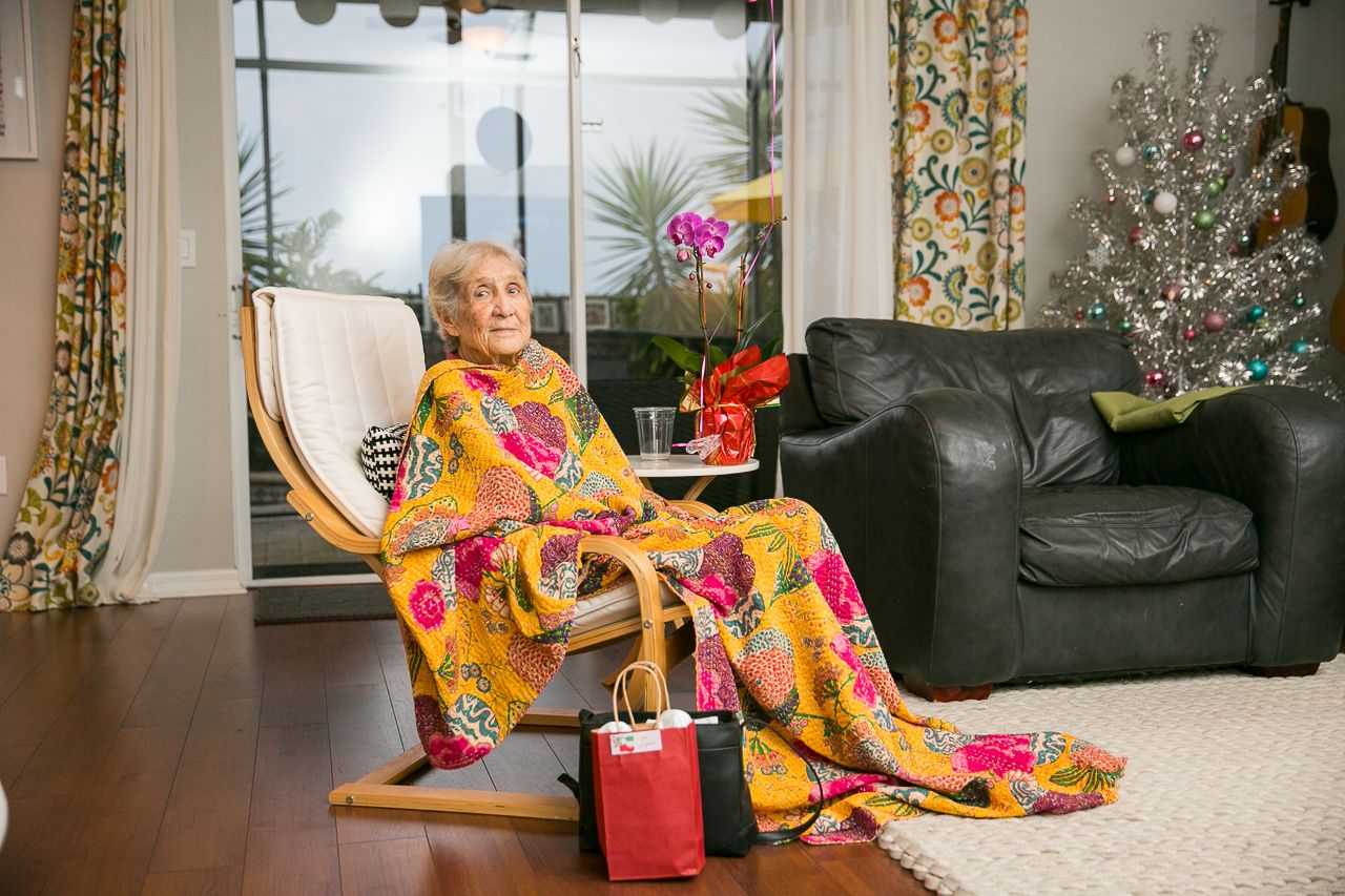 Elderly person relaxing in rocking chair wearing colorful floral dress with shopping bags nearby.
