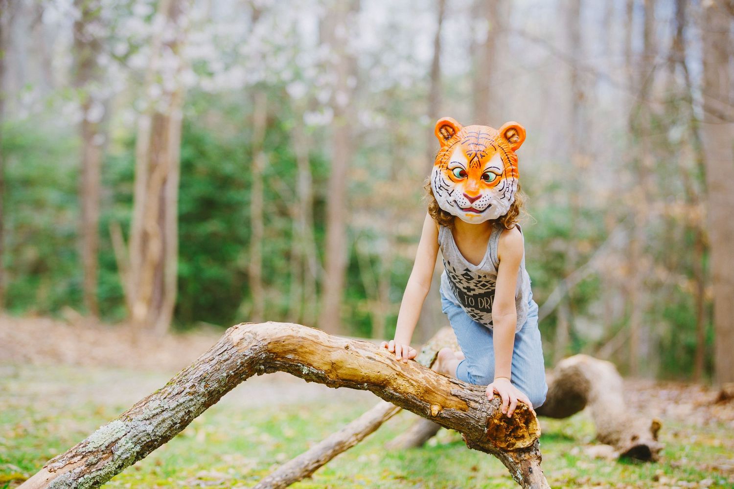 Tiger-masked figure playfully climbing on a fallen log in the woods.