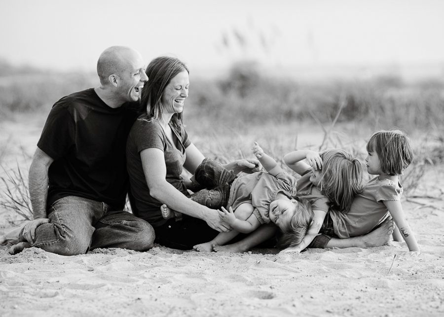 A family relaxes together on a beach in black and white during a casual photo session.