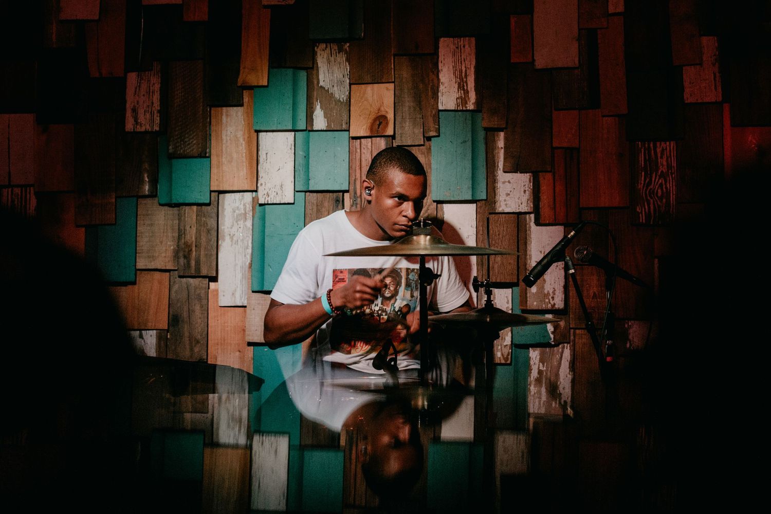 A drummer performs on stage against a geometric backdrop of turquoise and brown wooden panels.