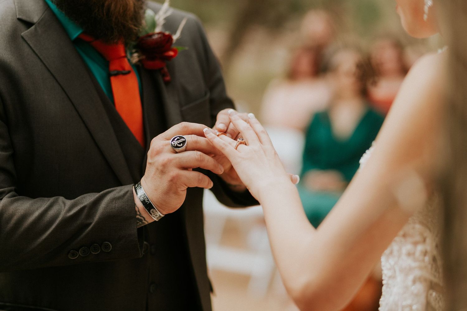 Close-up of wedding ceremony ring exchange with groom in black suit and red tie.