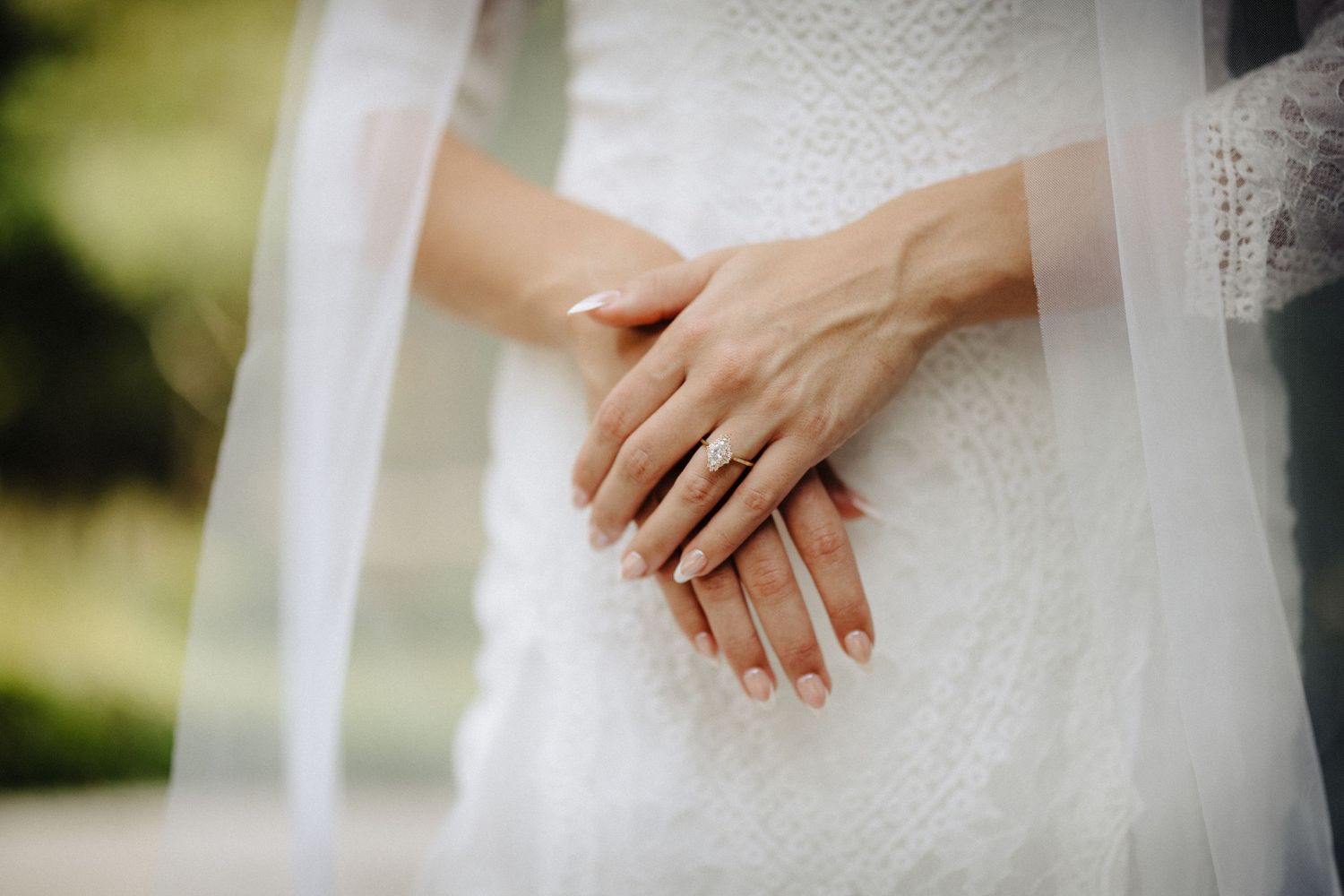 Close-up detail shots of hands delicately touching white lace wedding dress fabric in natural outdoor lighting.