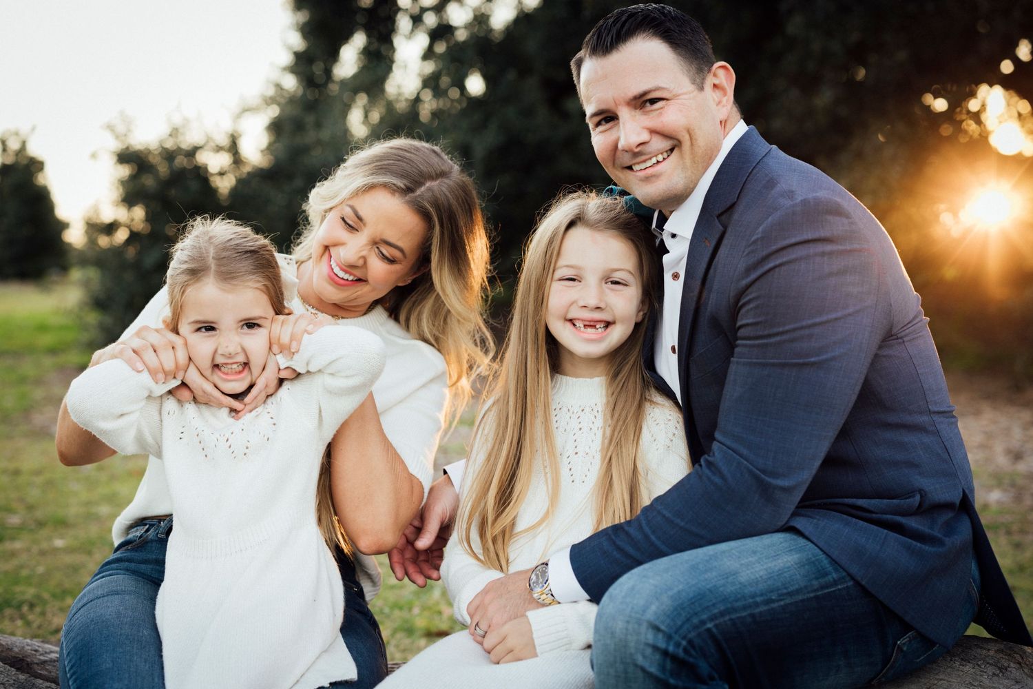 A family of four sits together outdoors during golden hour sunset.