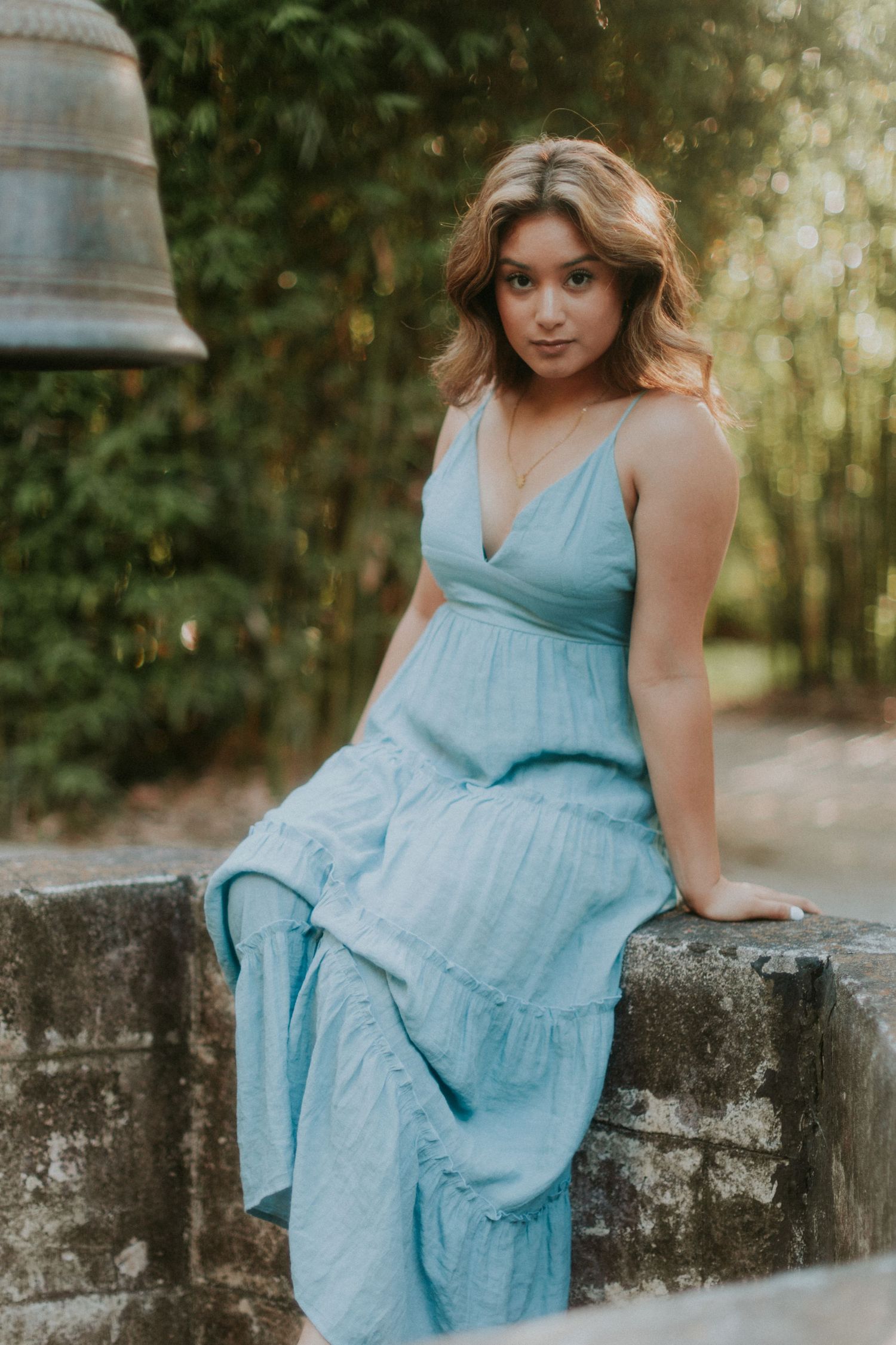 Portrait of someone in a light blue tiered maxi dress sitting on stone wall.