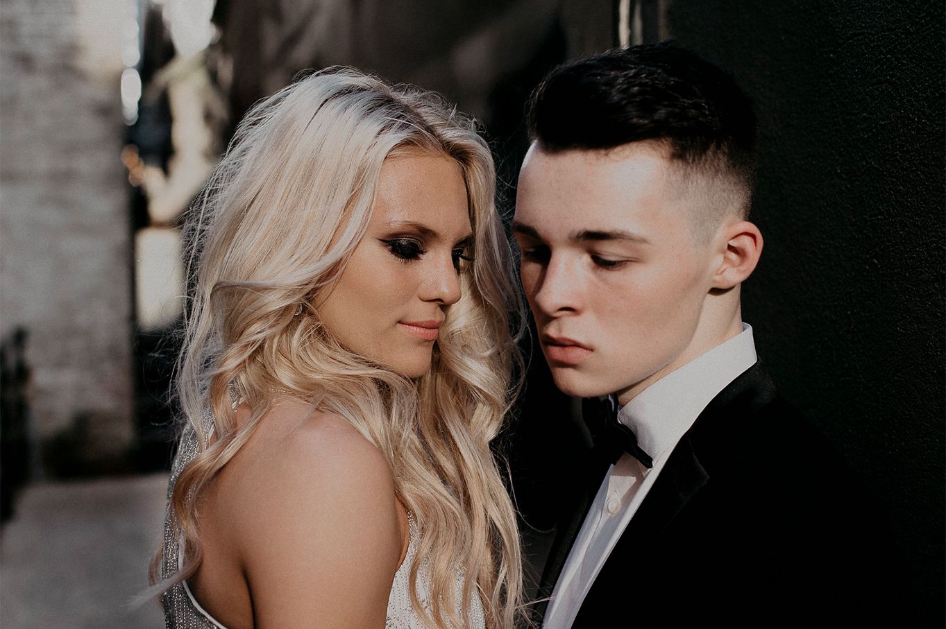 Romantic couple portrait with bride in sparkly dress and groom in black suit against dark background.