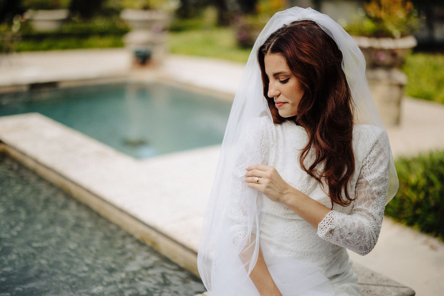 A person in a white dress sits elegantly by a modern swimming pool on a sunny afternoon.