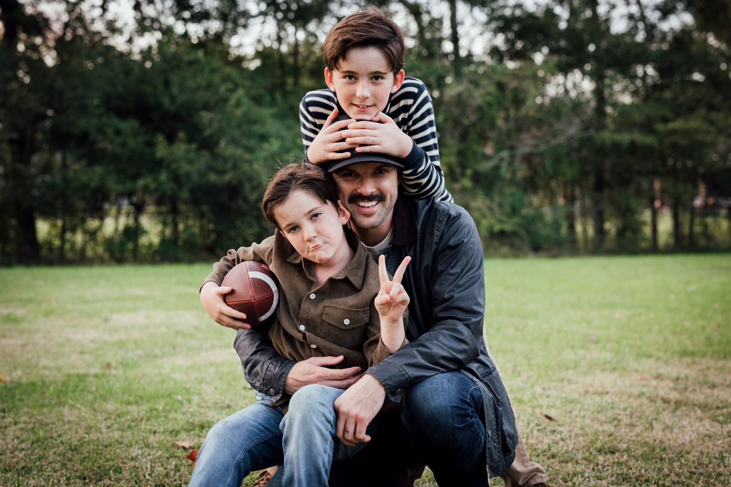 Three people playfully posing with football outdoors on grassy field.