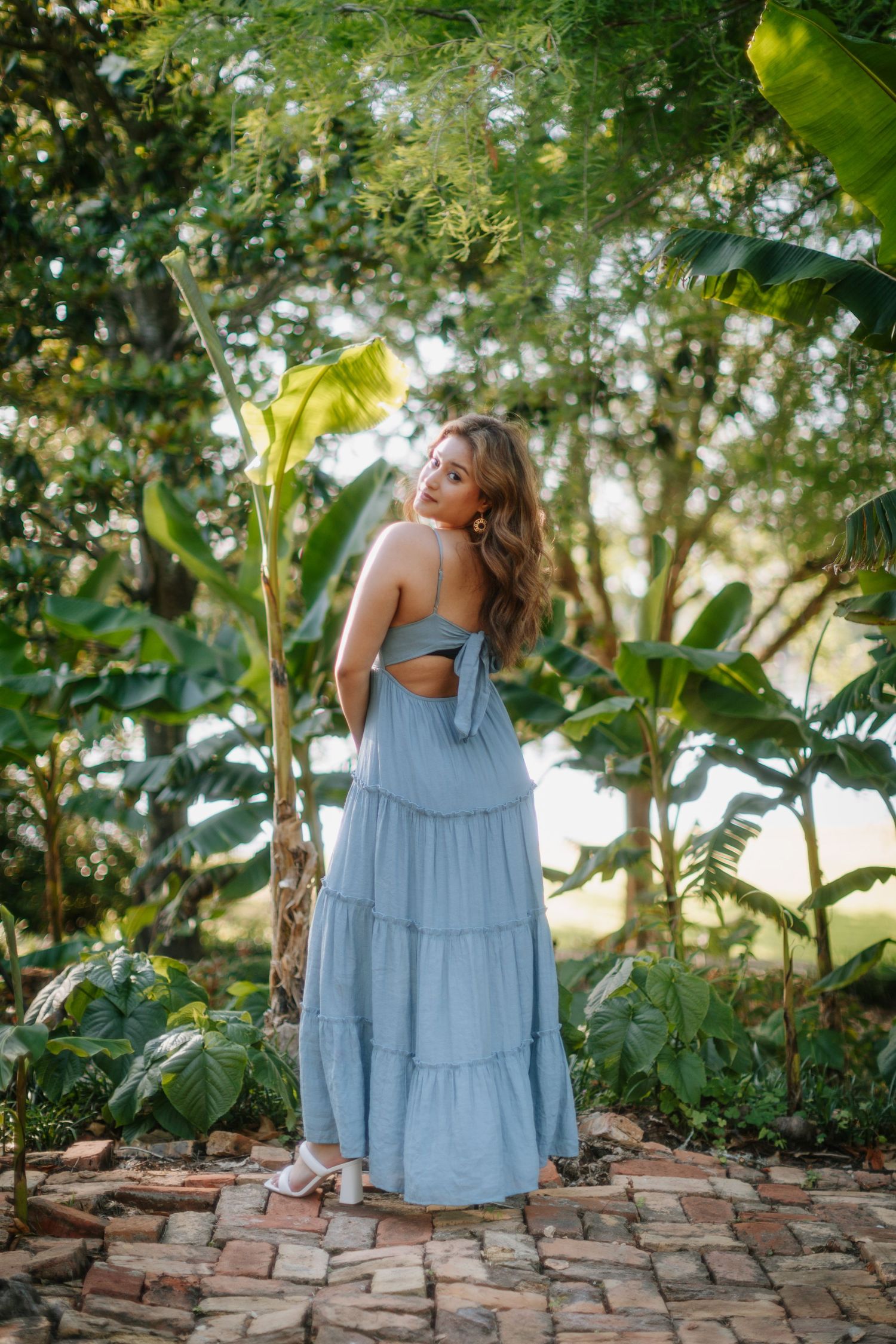 Blue dress flowing in a lush tropical garden setting with brick pathway.