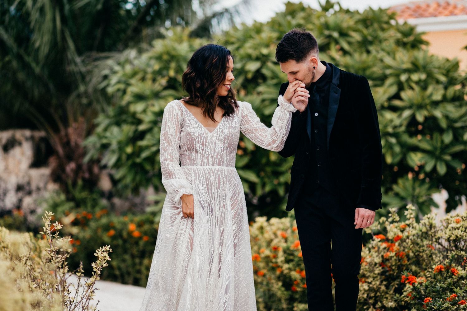 A couple shares romantic moments in a lush garden setting with terracotta roofing visible in the background.