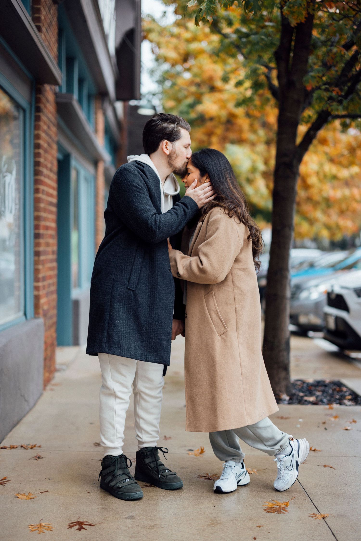 A tender autumn street scene showing an intimate moment between two people in coats.