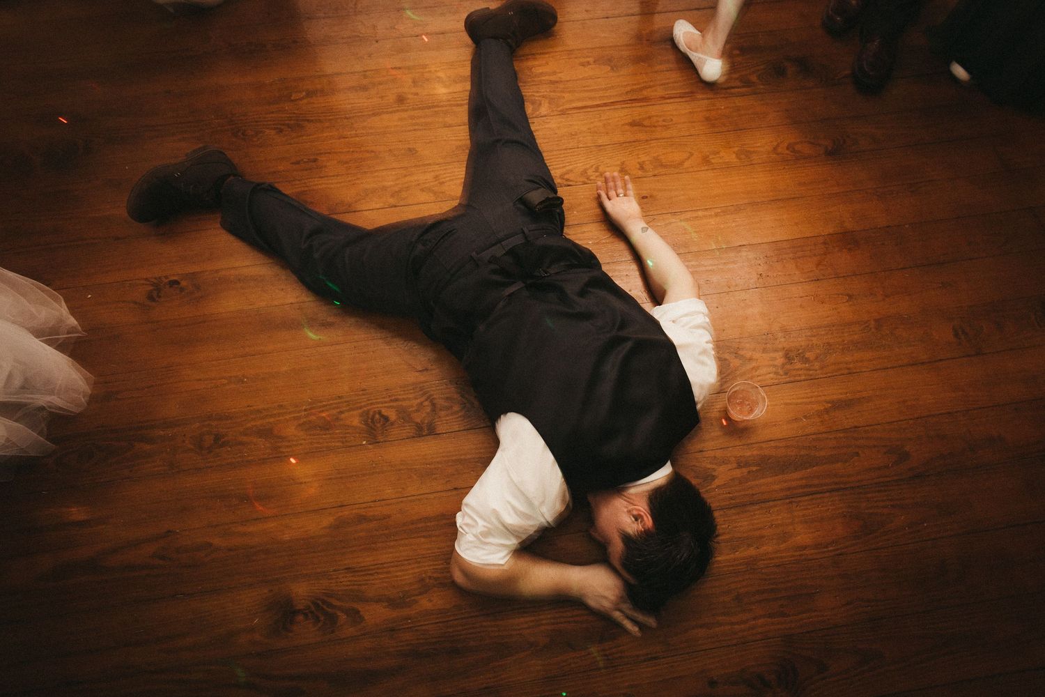 Person lying face down on a wooden floor in black clothing.