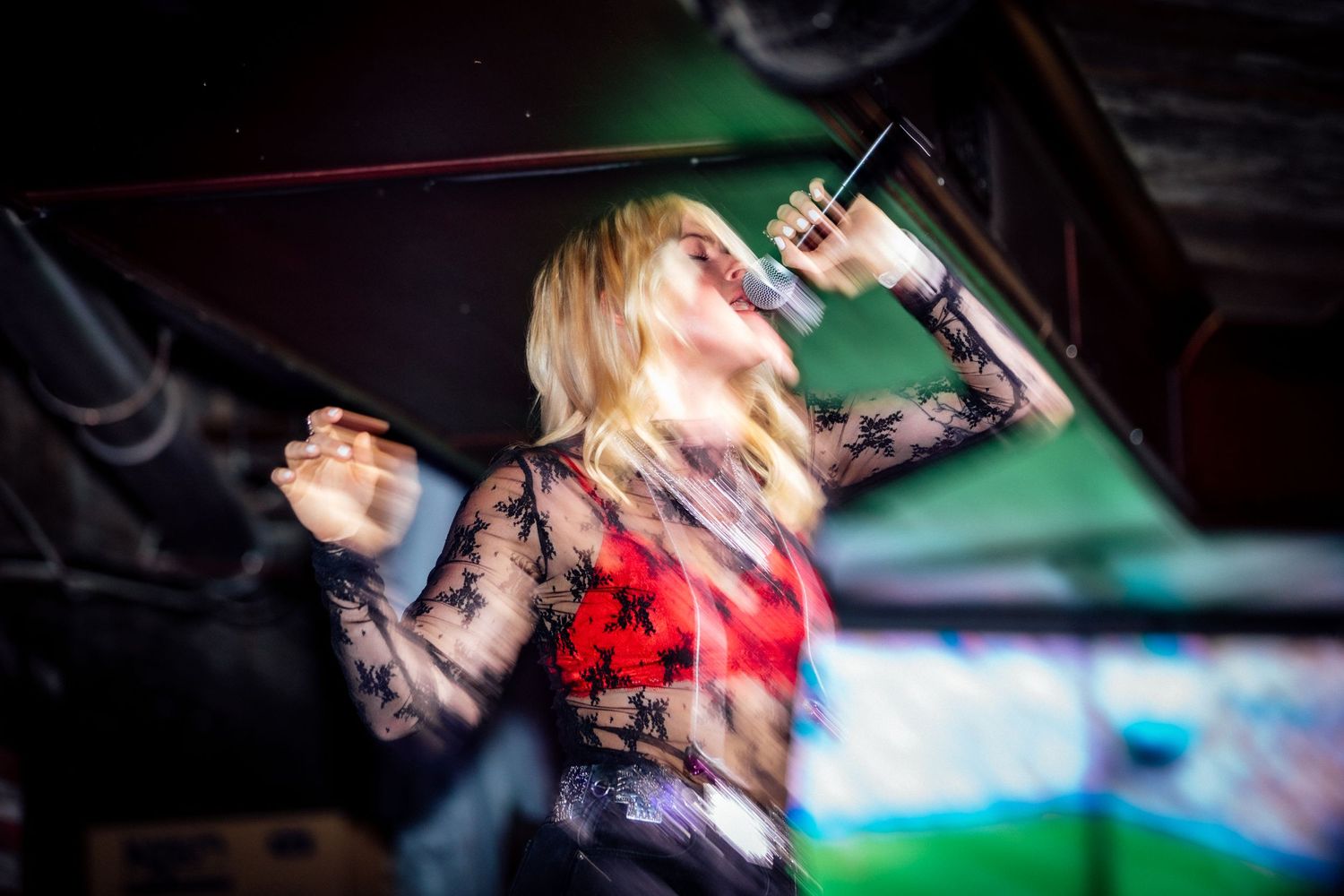 Concert performer singing and dancing energetically under colorful stage lights.