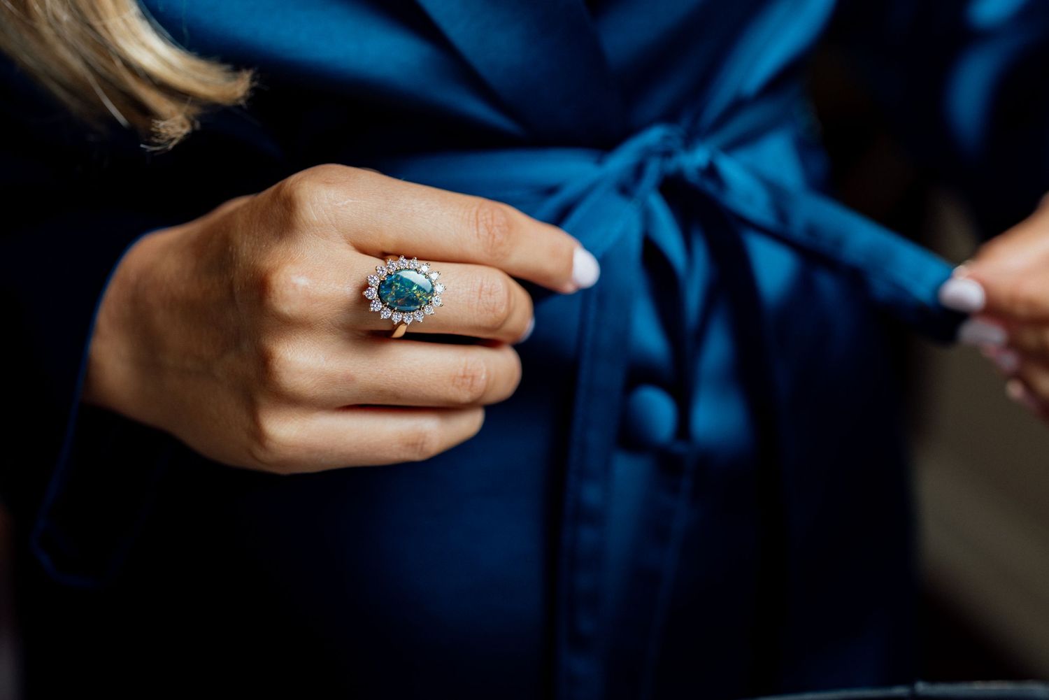 Close-up of hand wearing elegant blue turquoise ring against navy blue fabric.