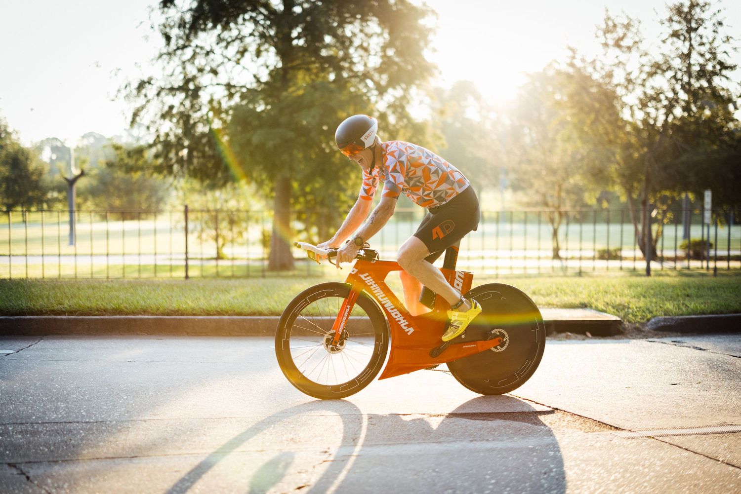 Cyclist on aerodynamic bike silhouetted against golden sunset on paved path.