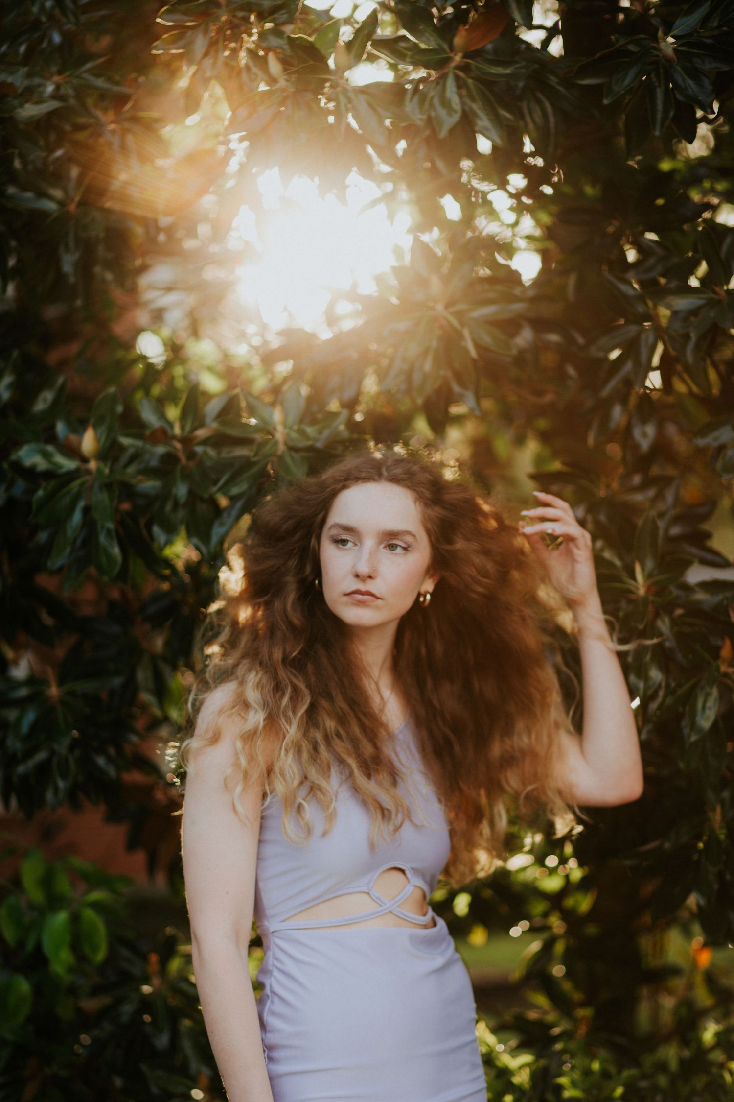 Fashion portrait with sunlight streaming through leaves in a garden setting.