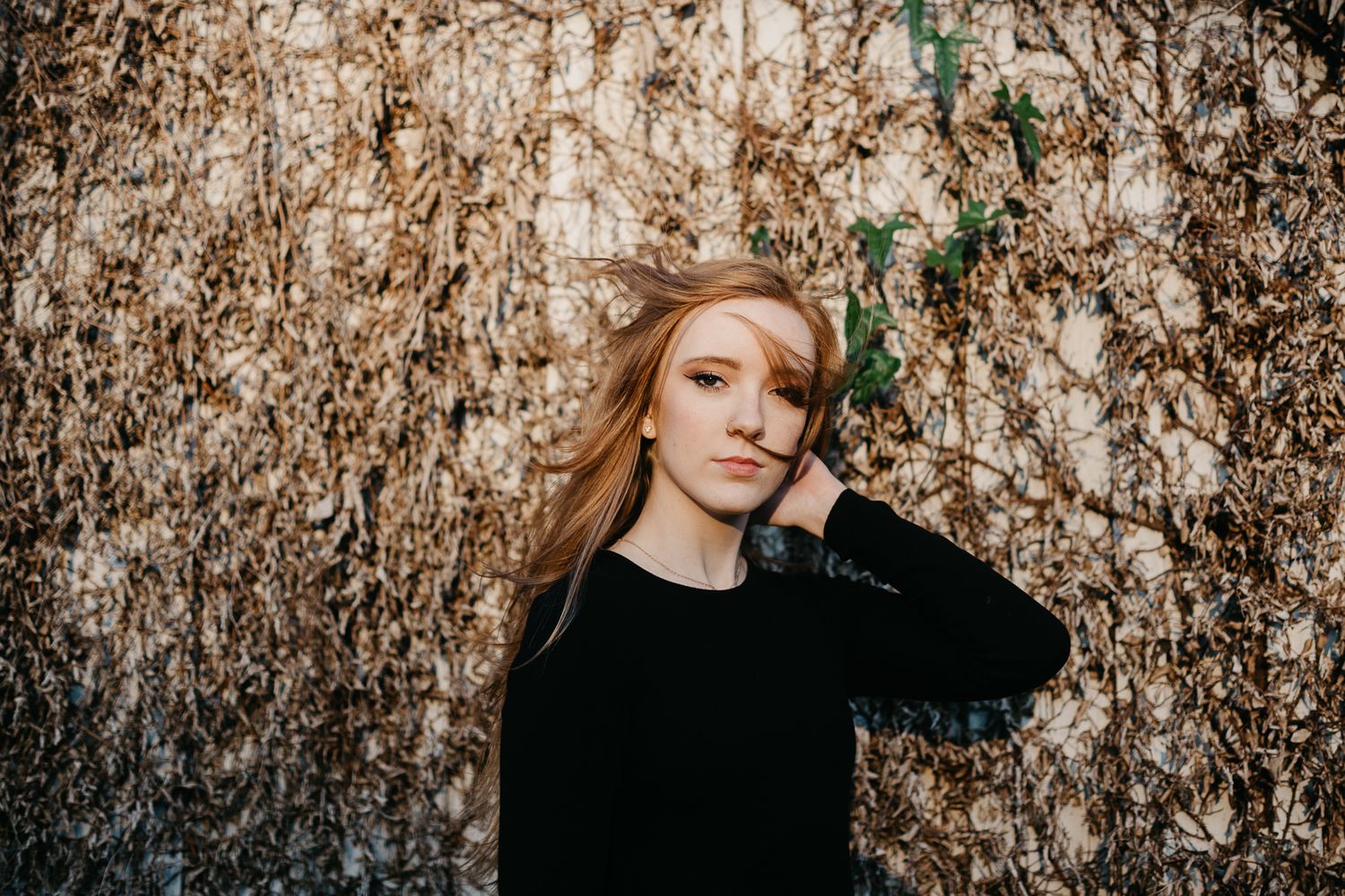 Portrait against textured wall with blonde hair and black sweater in moody lighting.