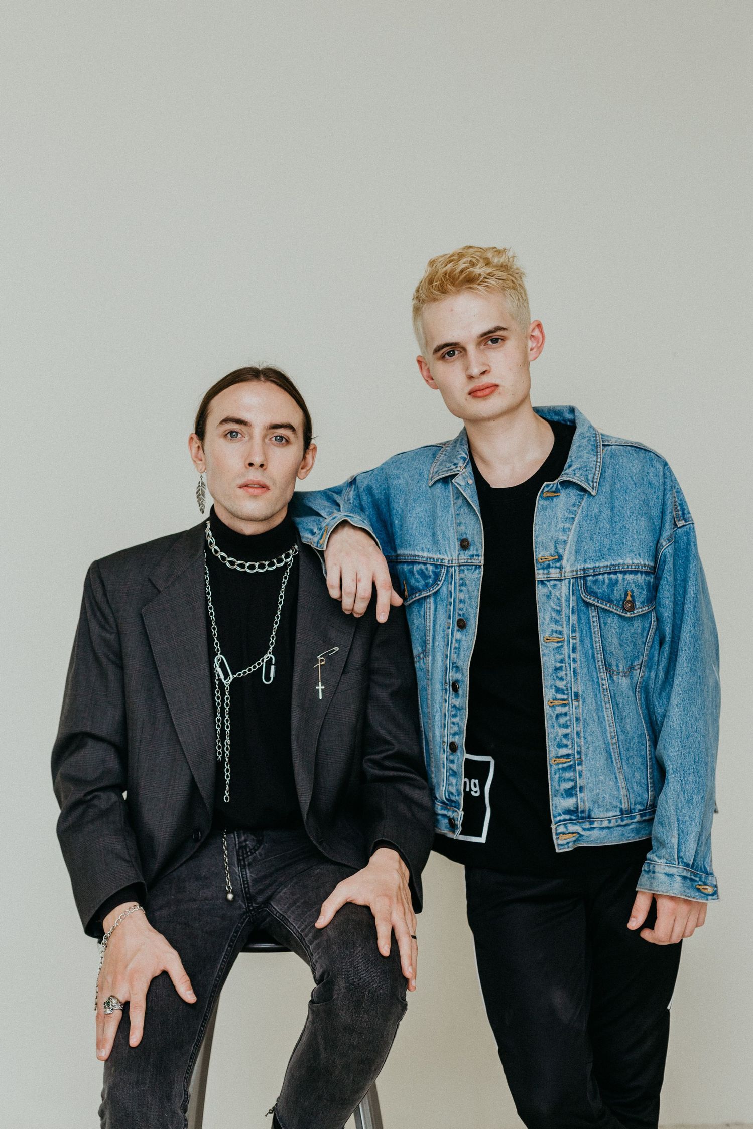 Two models pose in contrasting outfits featuring a dark blazer and denim jacket against a light background.