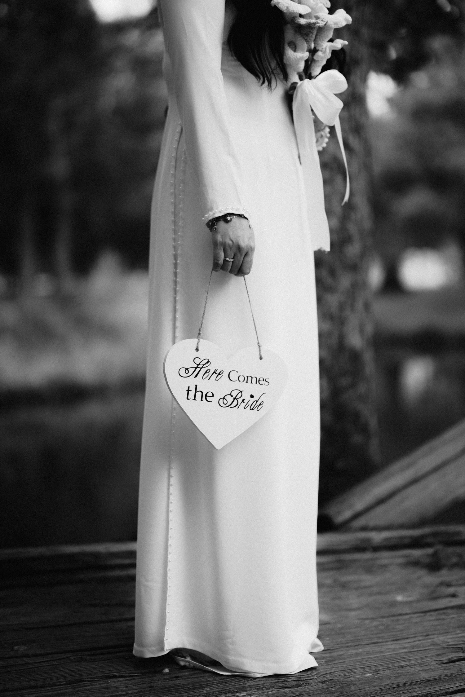 Black and white wedding photo showing dress detail with 'Here comes the bride' text on decorative signs.
