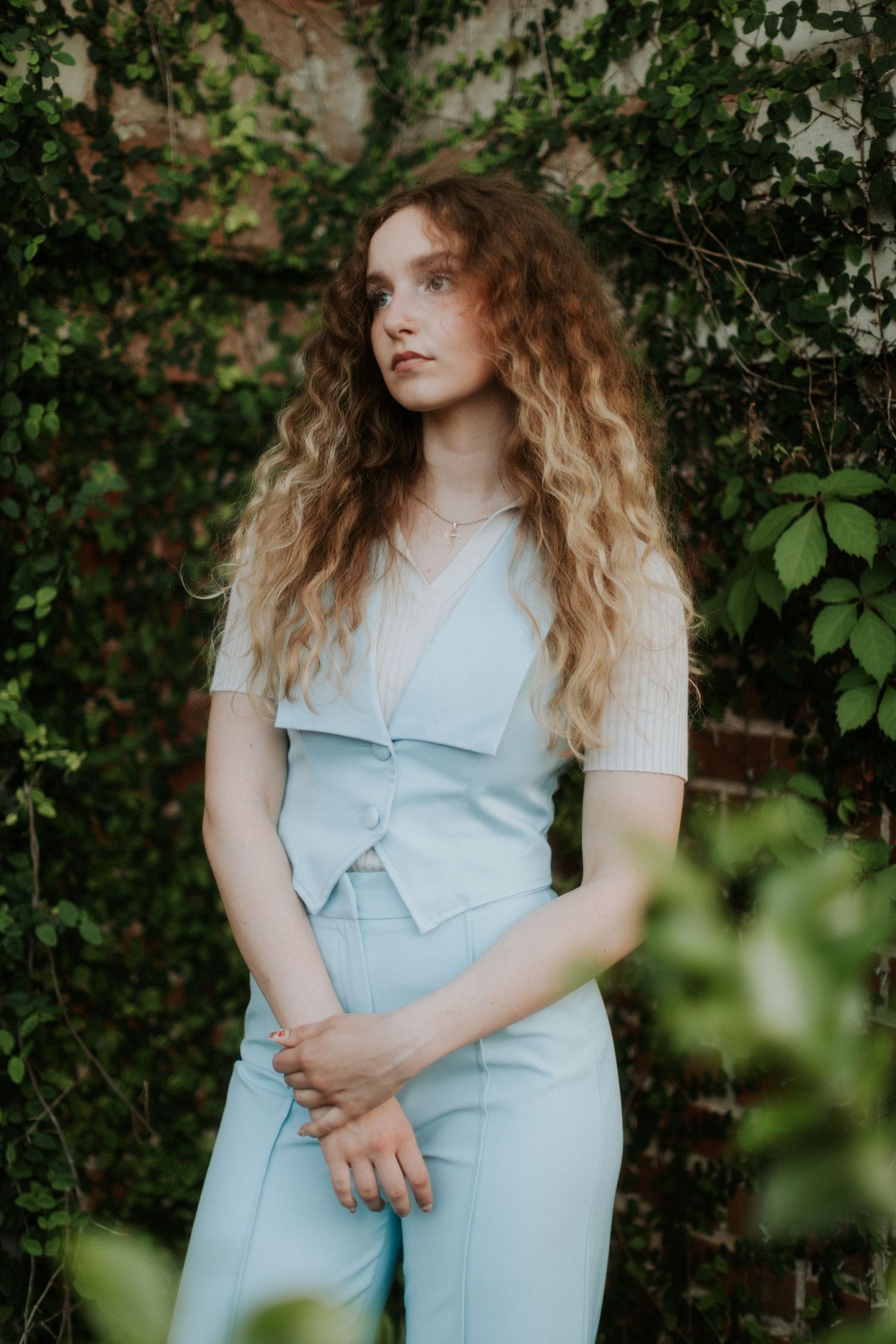 Dreamy outdoor portrait featuring pale blue vintage-style outfit against ivy-covered brick wall.