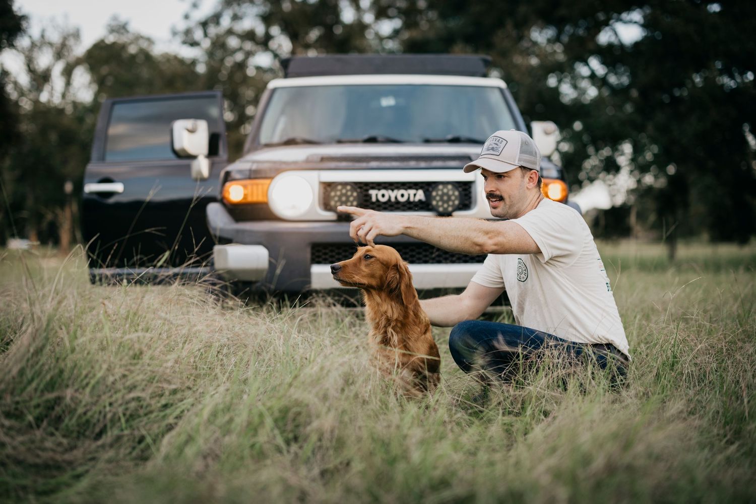 Person petting golden retriever in front of Toyota truck with headlights on at dusk.
