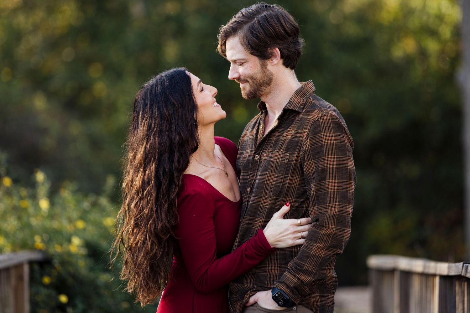 Romantic outdoor portrait of couple in casual attire surrounded by greenery.