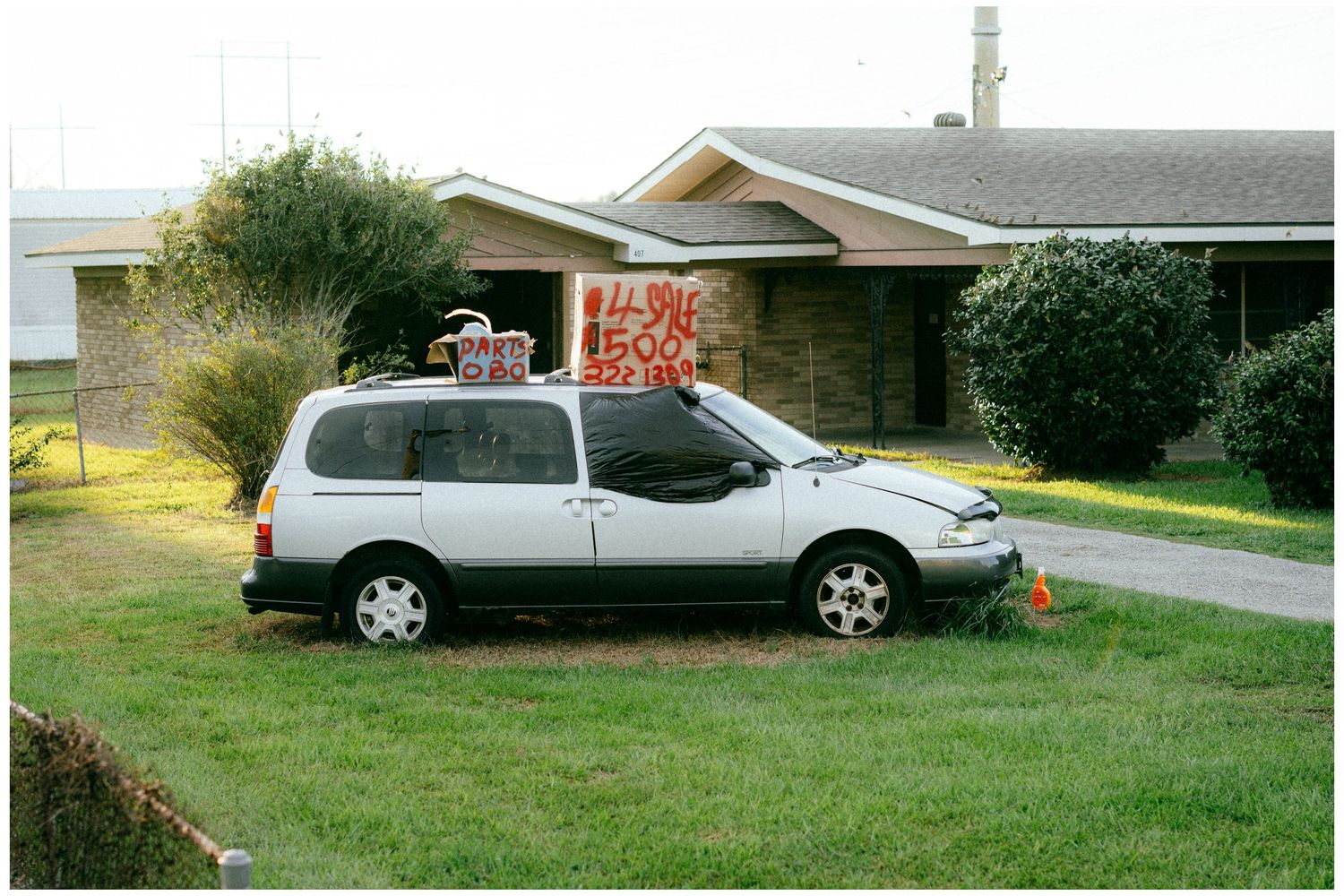 Grey minivan parked in front of suburban house with brick accents.