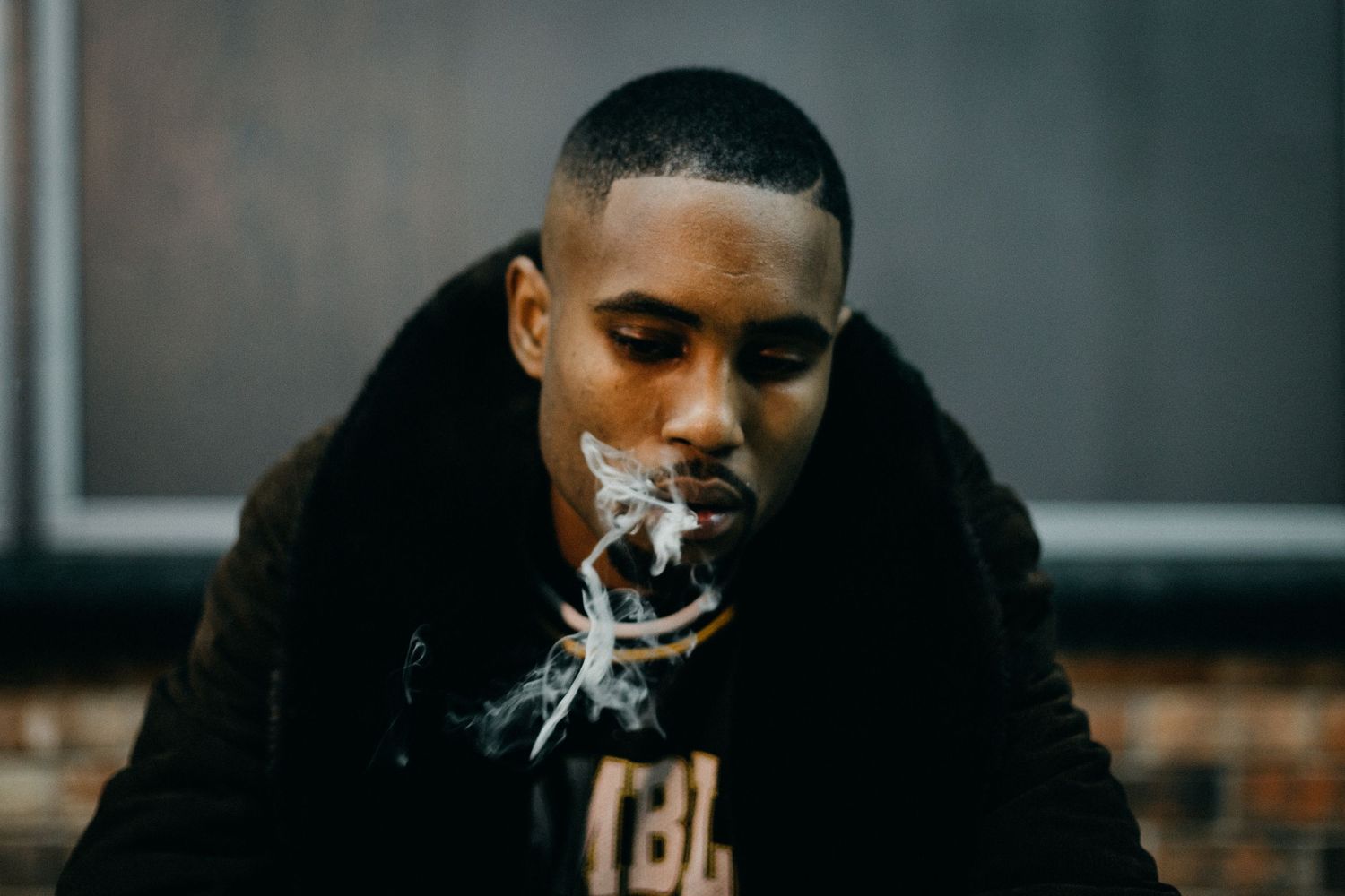 Artistic portrait of someone exhaling smoke while wearing a dark coat indoors.