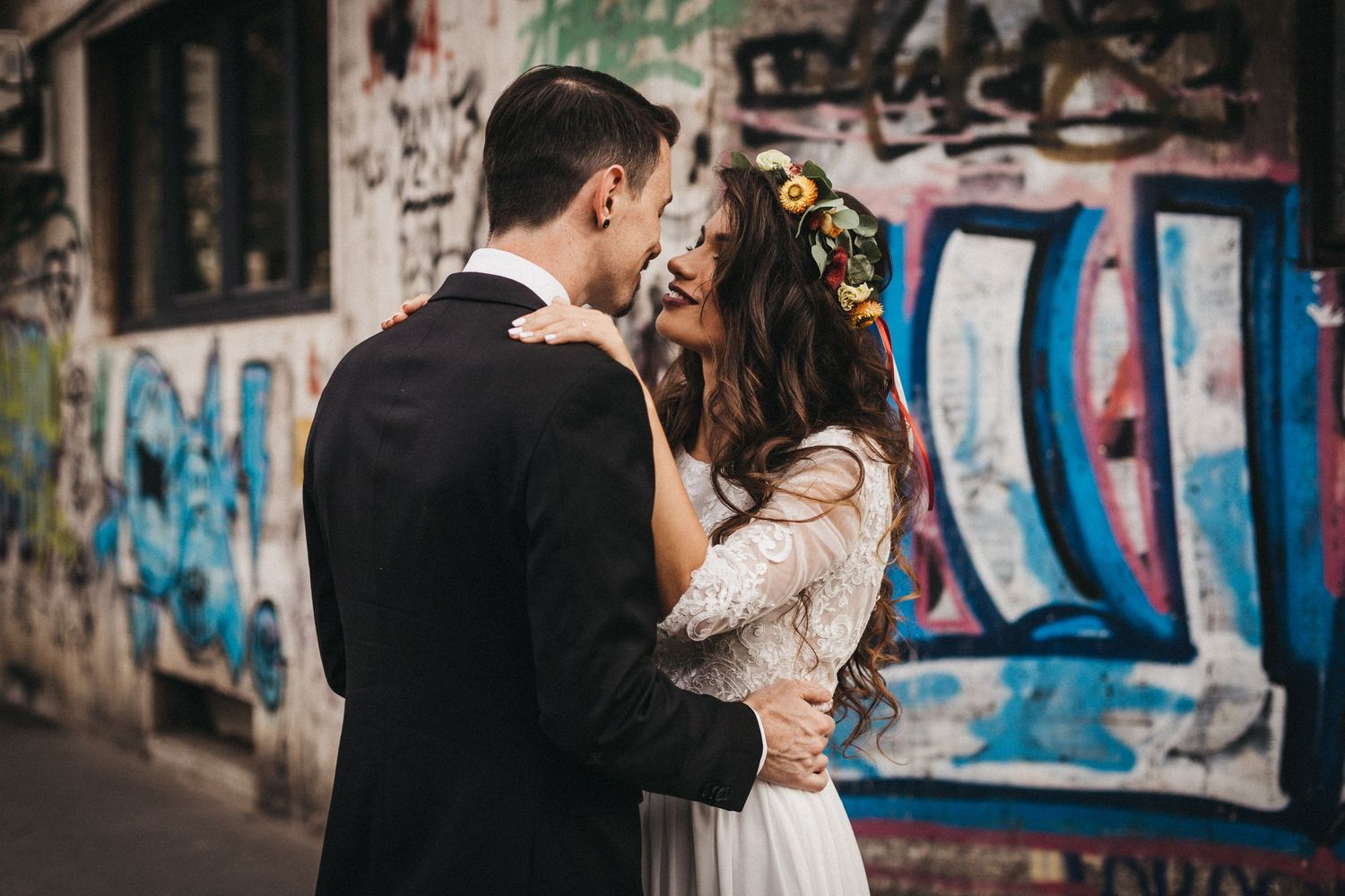Romantic wedding couple embraces in front of colorful street art and graffiti backdrop.