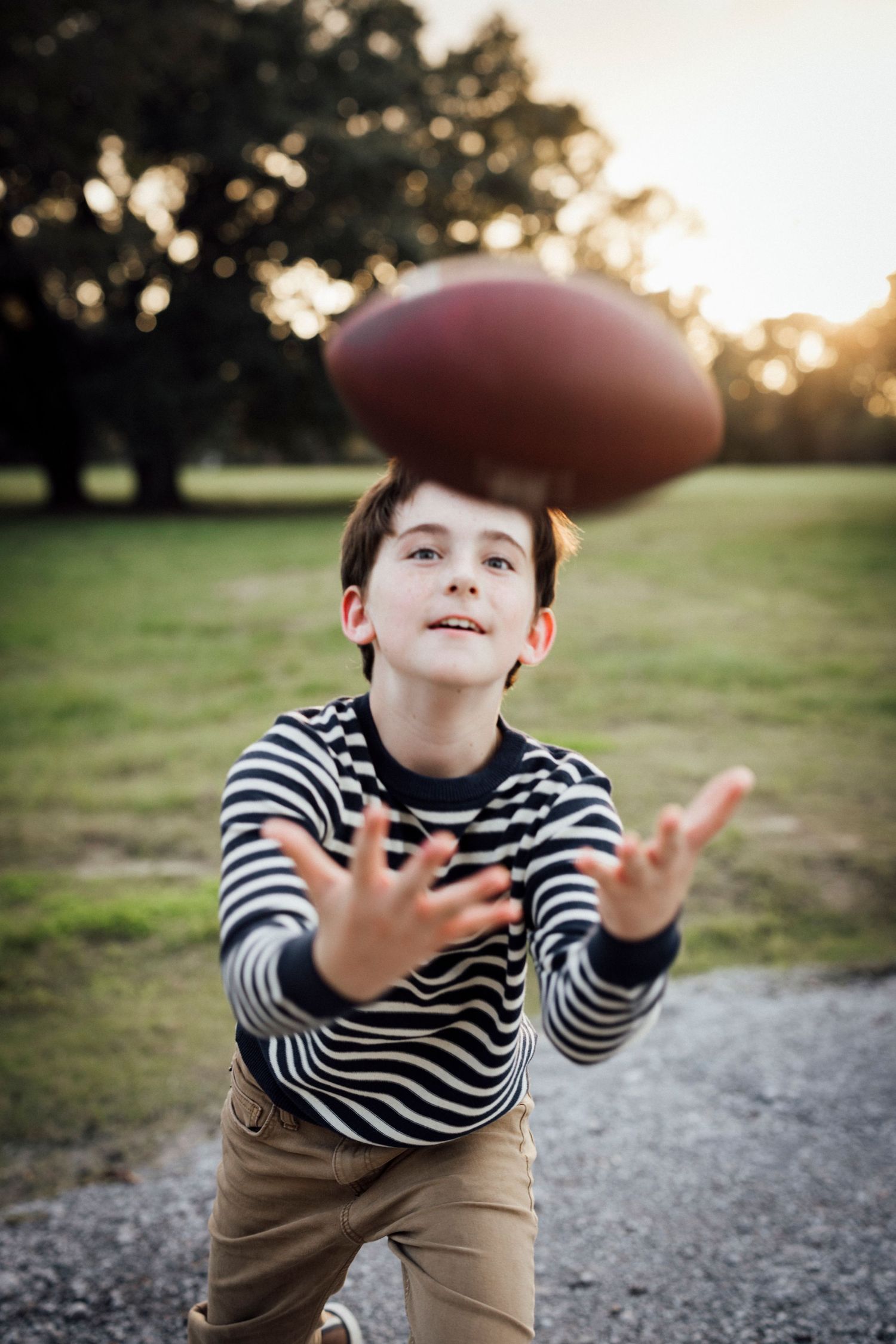 A child in a striped shirt catches a football at sunset.
