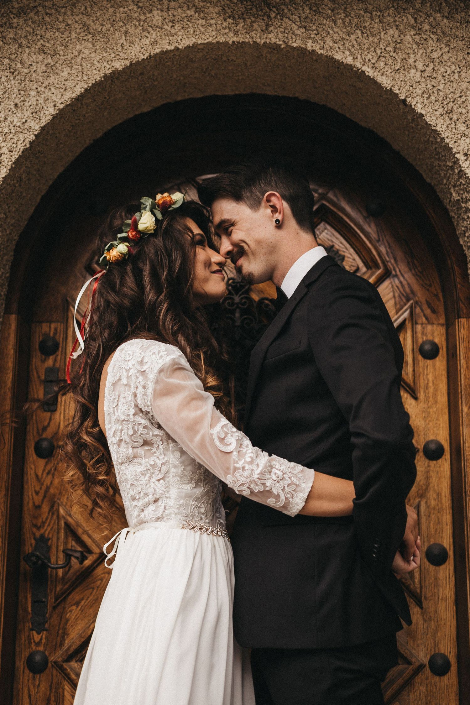 Wedding couple shares romantic moment under wooden arched doorway.