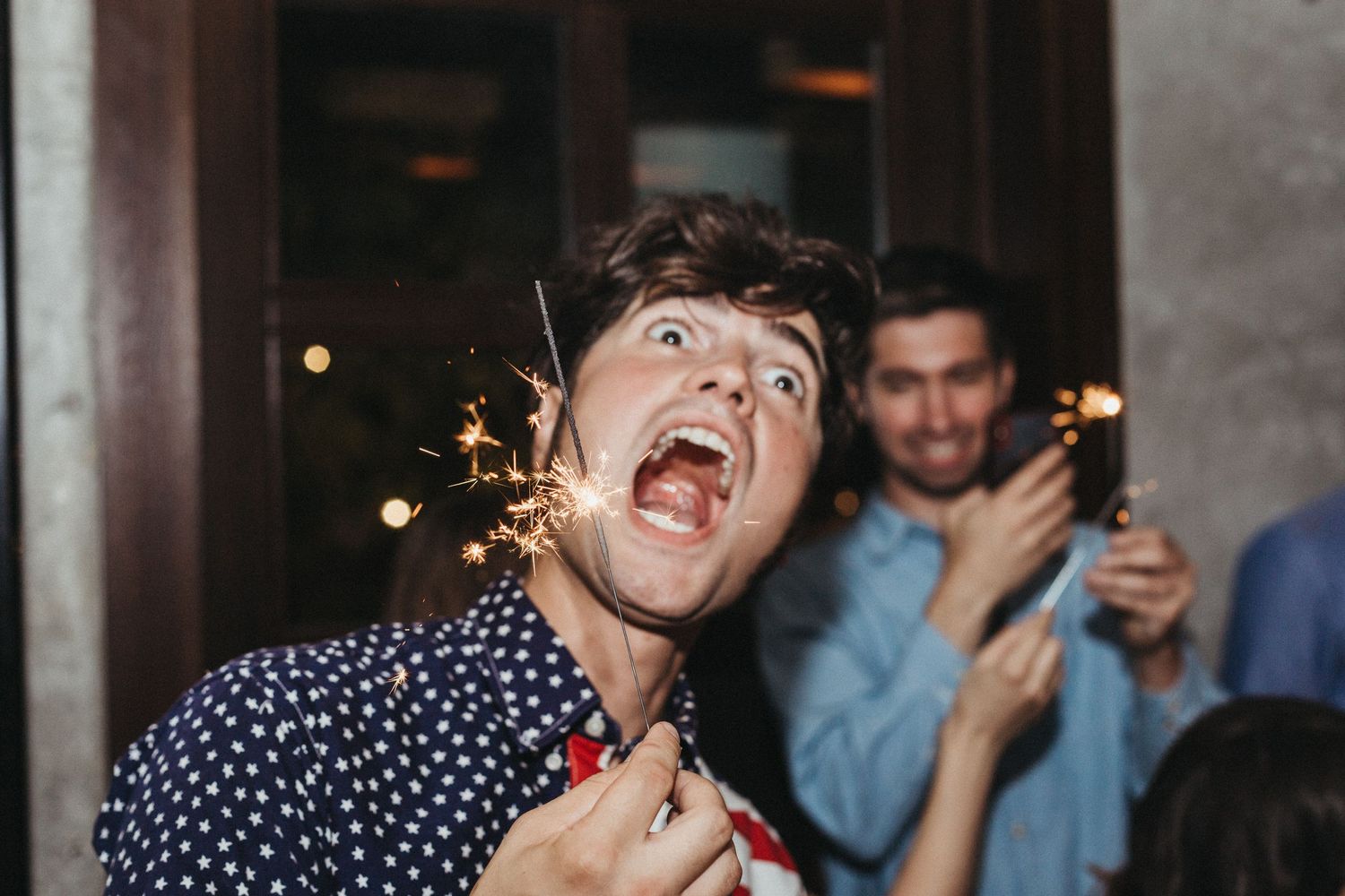 Party guest reacting excitedly while holding a sparkler at night.