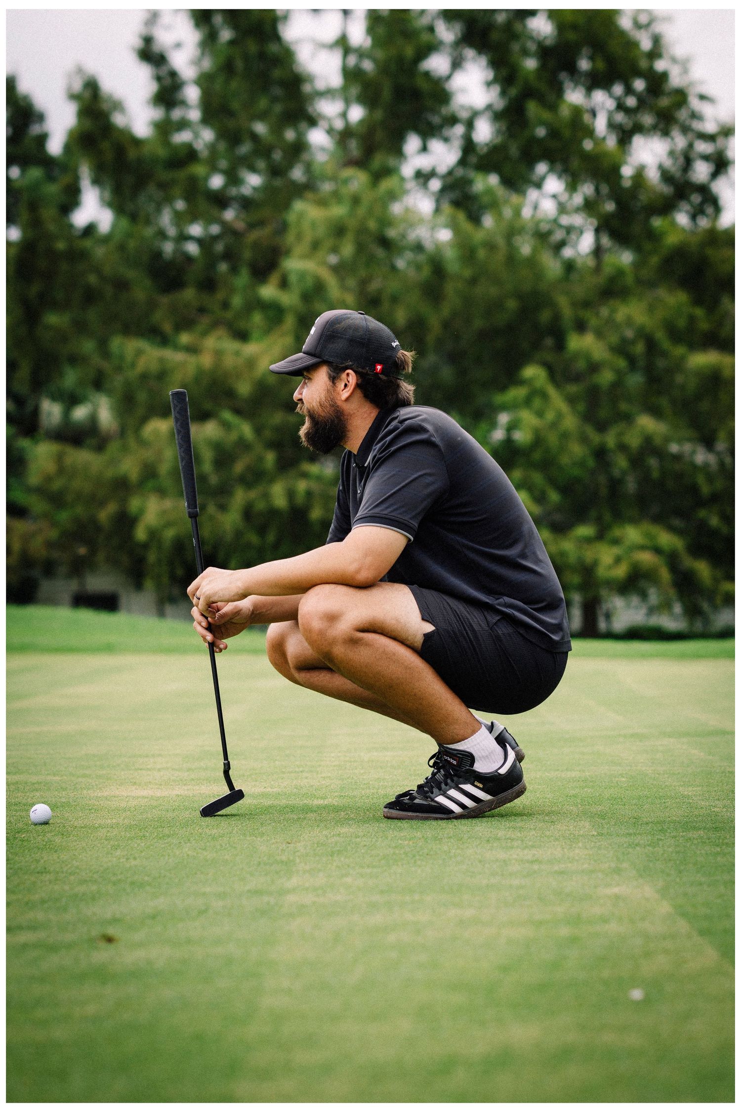 Golfer in black outfit crouching to read green on putting surface.