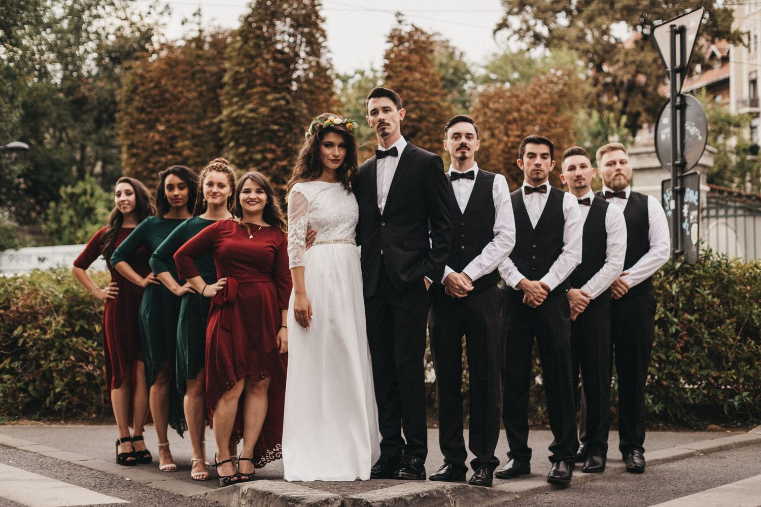 Wedding party poses outdoors with bridesmaids in green dresses and groomsmen in black vests.