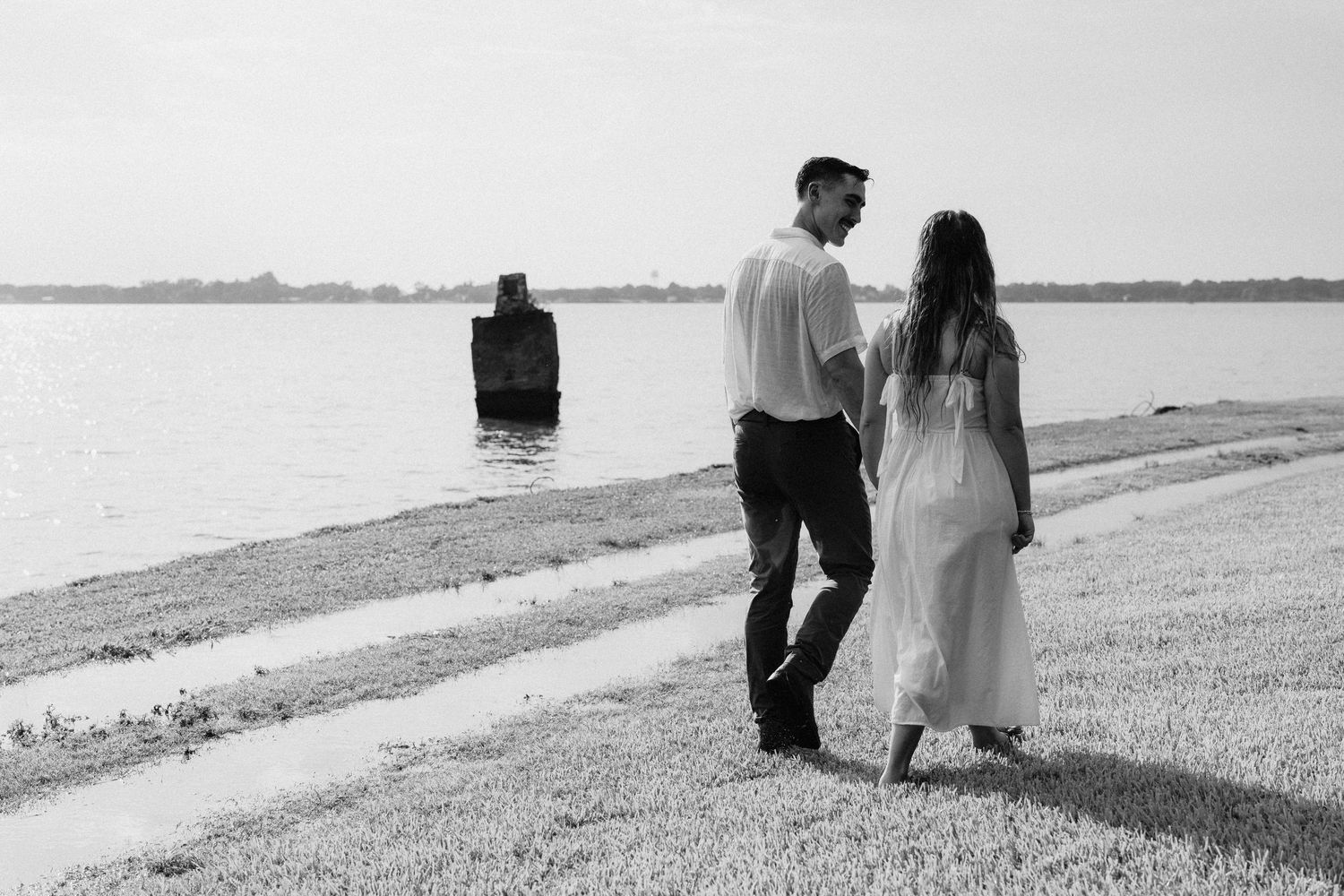 A romantic couple walks along a scenic beach shoreline in black and white photography.