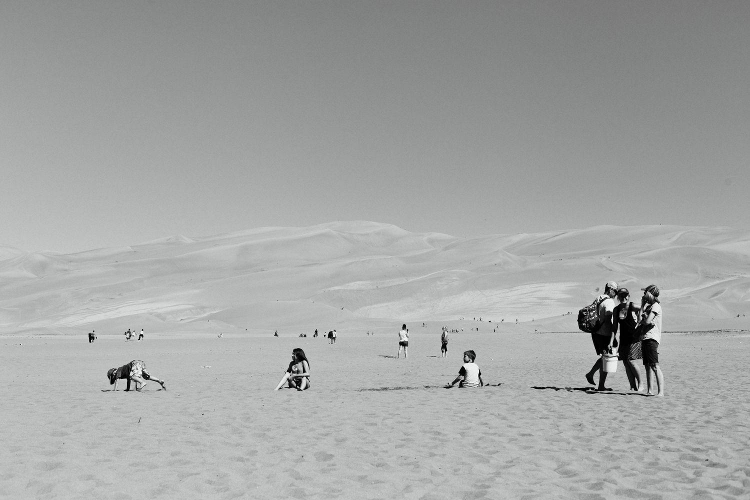 Black and white photo of people enjoying leisure time on sand dunes under a cloudy sky.