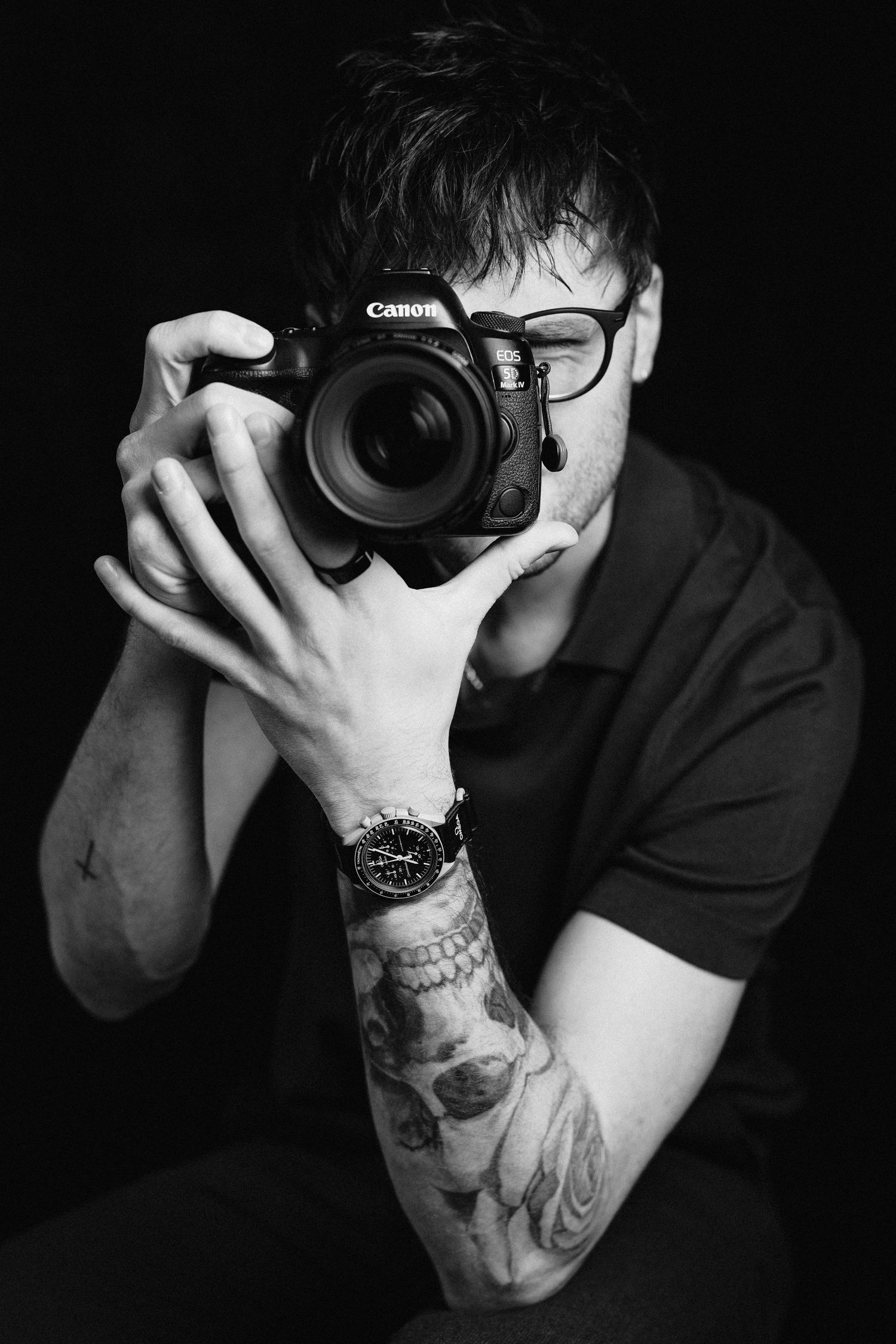 Photographer with tattoos taking photo with Canon camera in dramatic black and white portrait.