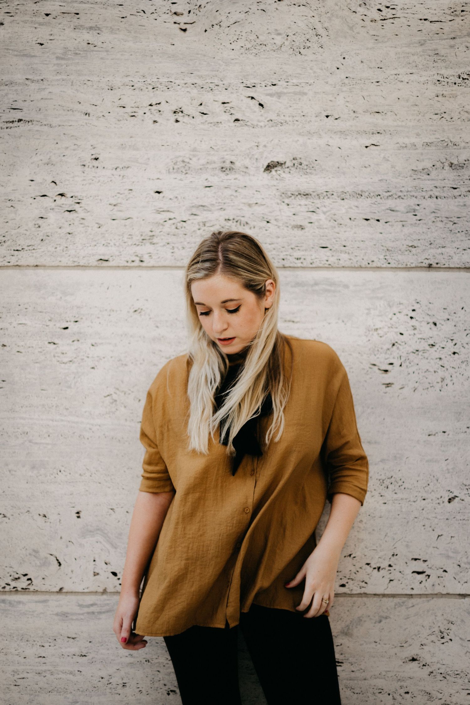 Fashion portrait against concrete wall wearing camel sweater and dark pants.