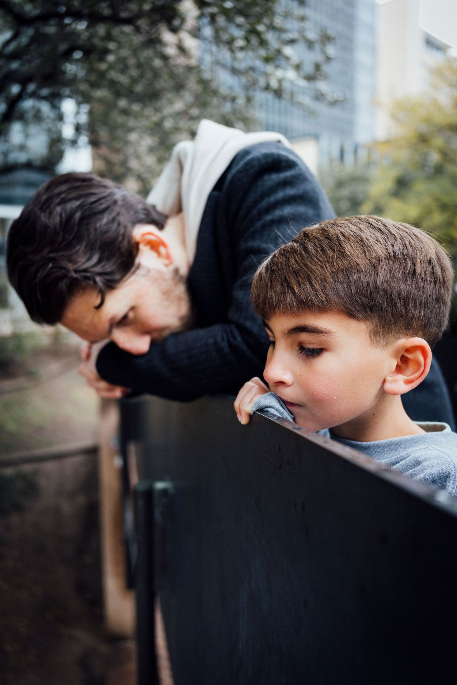 A parent and child lean against a dark surface outdoors.