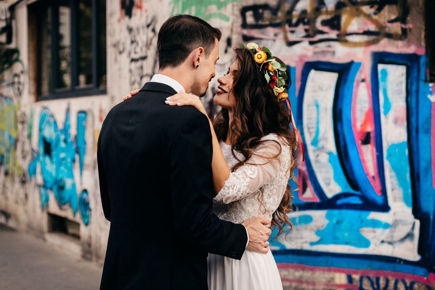 A couple shares a romantic kiss in front of a colorful graffiti wall during their wedding photo session.