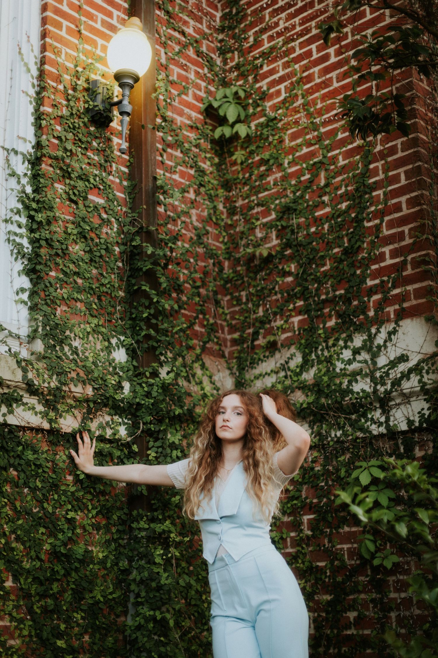 Artistic portrait against ivy-covered brick wall with vintage lamp post creating ethereal atmosphere.