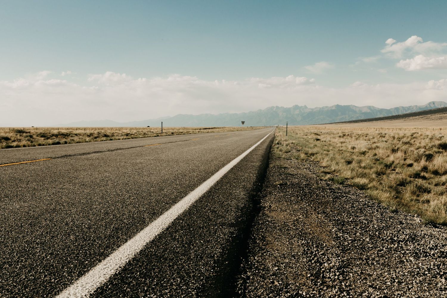 A long empty road stretches toward the horizon under blue skies in an arid landscape.