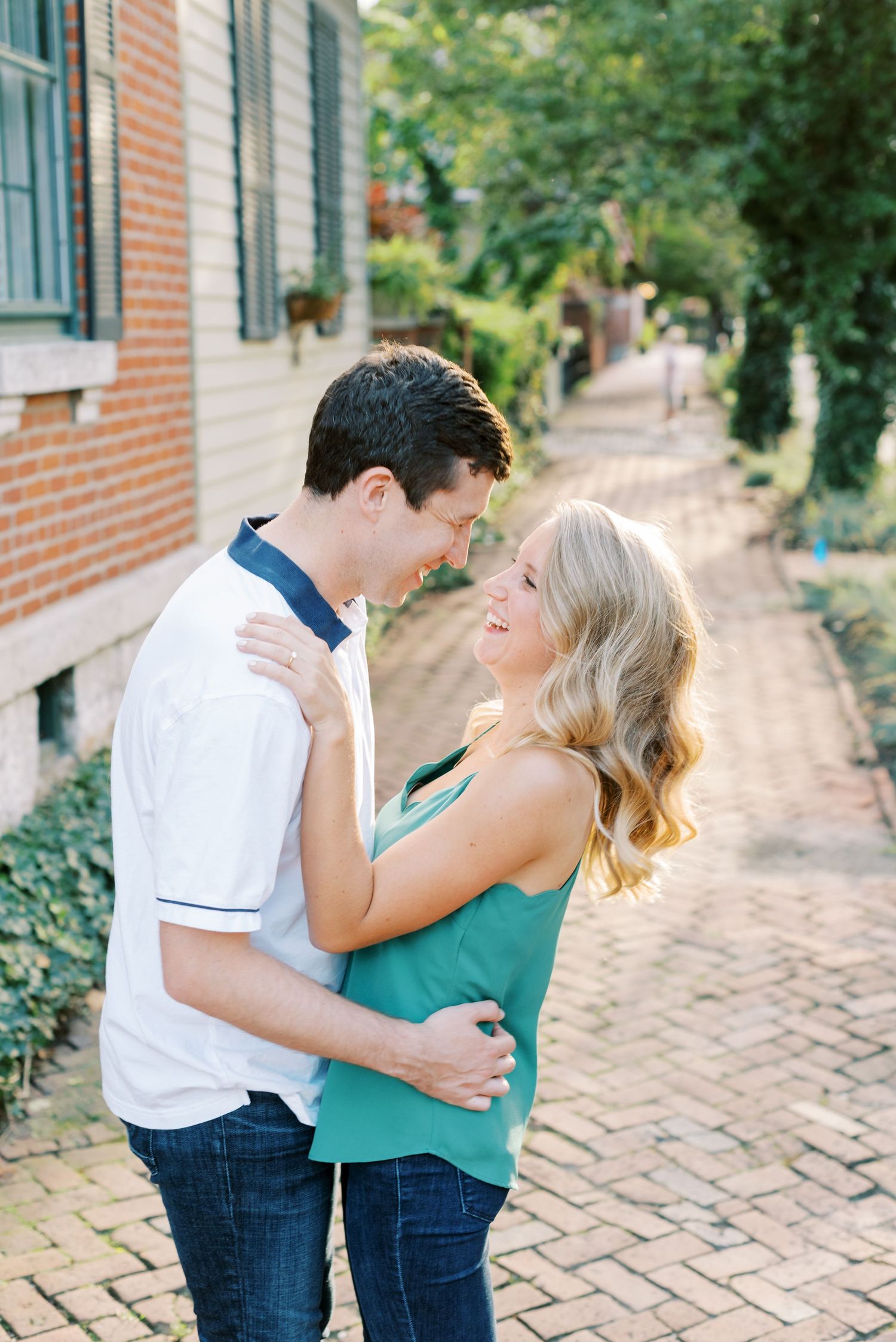 A couple shares romantic moments on a brick pathway surrounded by greenery and brick buildings.