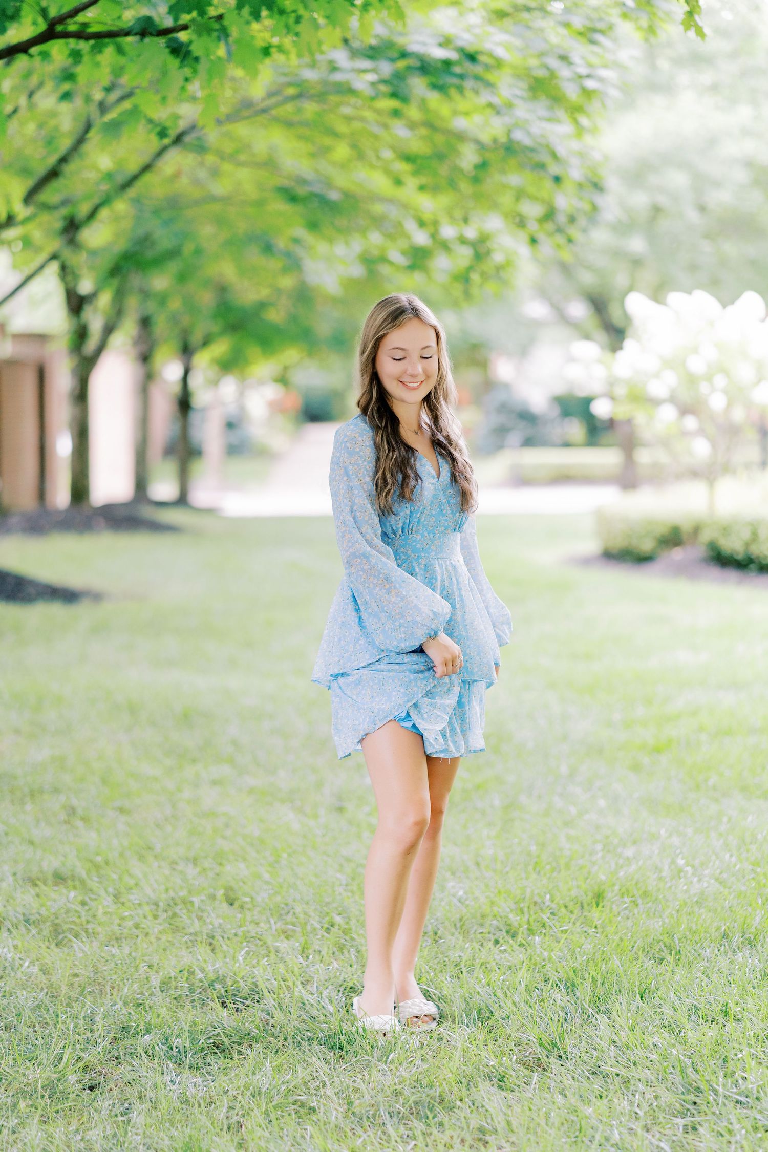 A light blue lace dress with bell sleeves is worn outdoors on a sunny spring day with green trees in the background.
