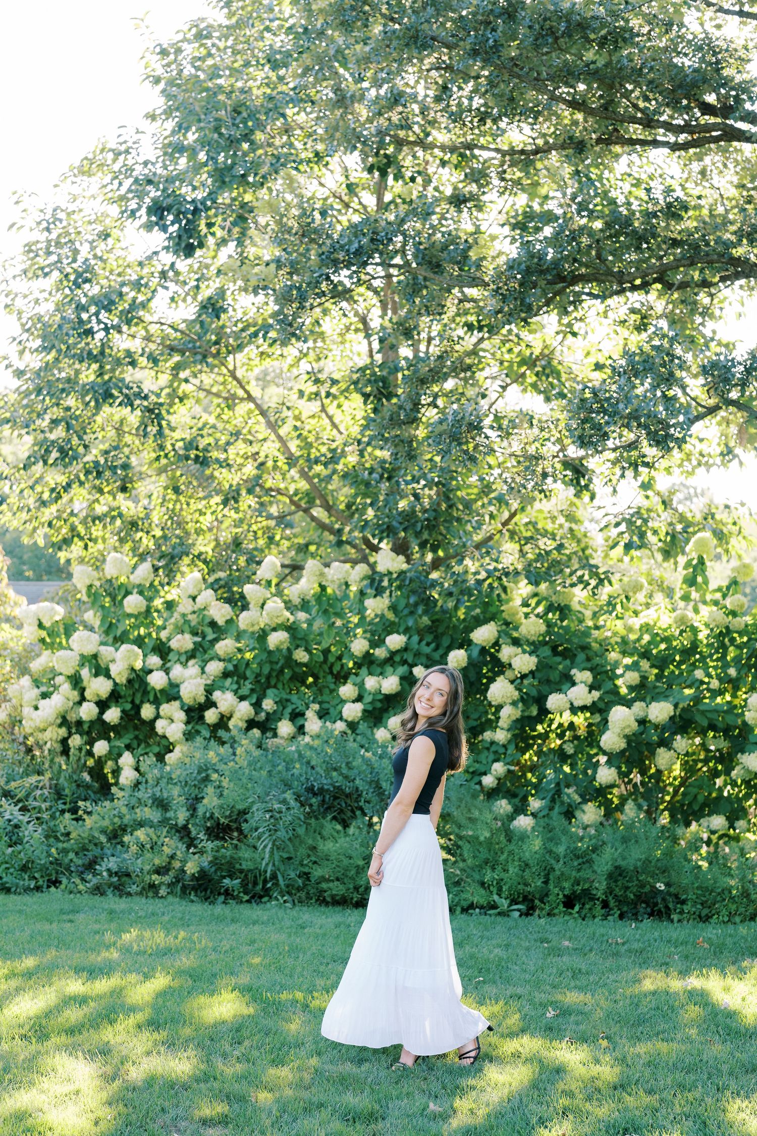 A couple shares a romantic moment in a sunlit garden with blooming white flowers and lush greenery.