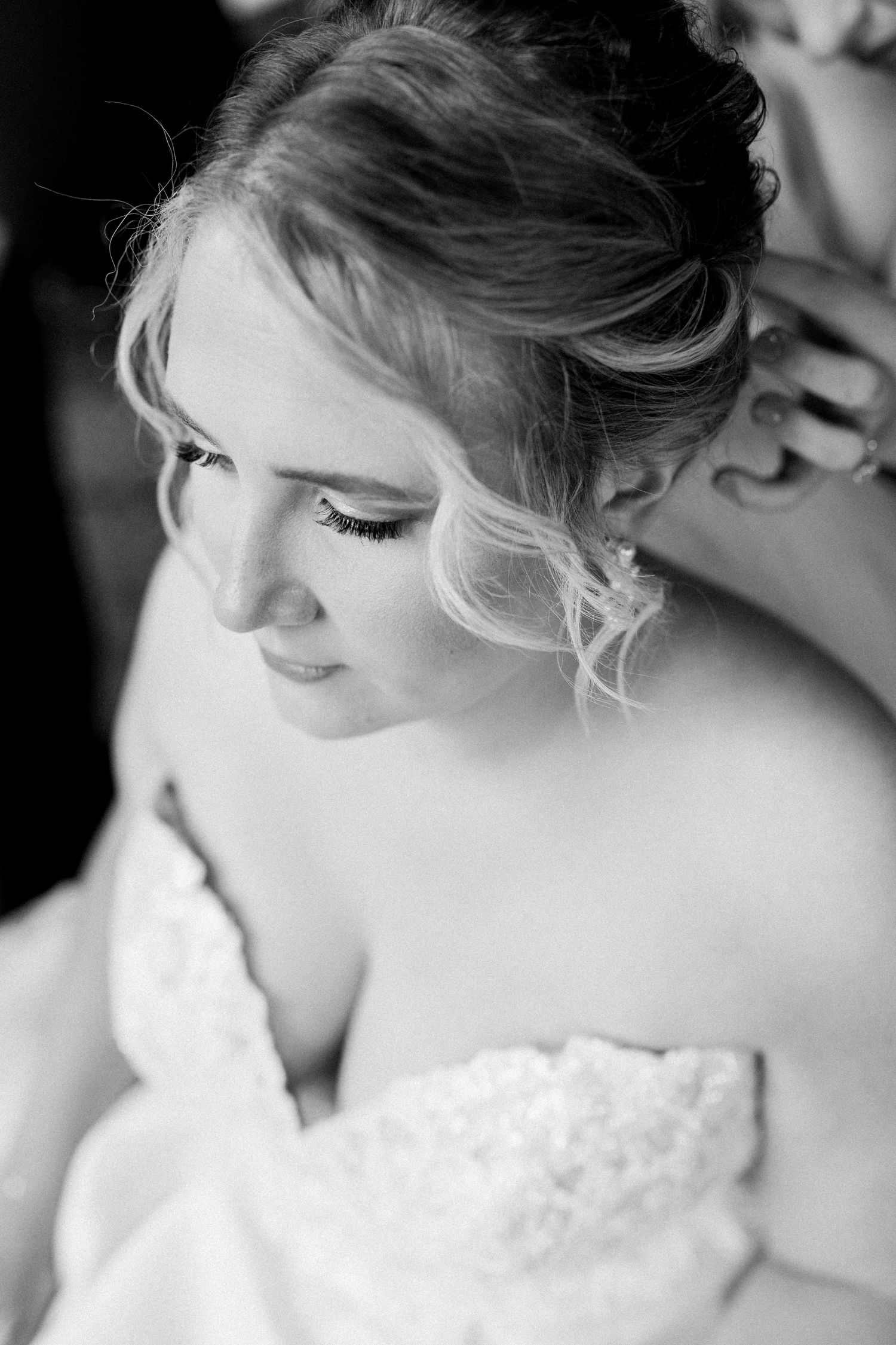 Black and white close-up portrait showing soft bridal makeup and an elegant updo hairstyle with wispy strands.