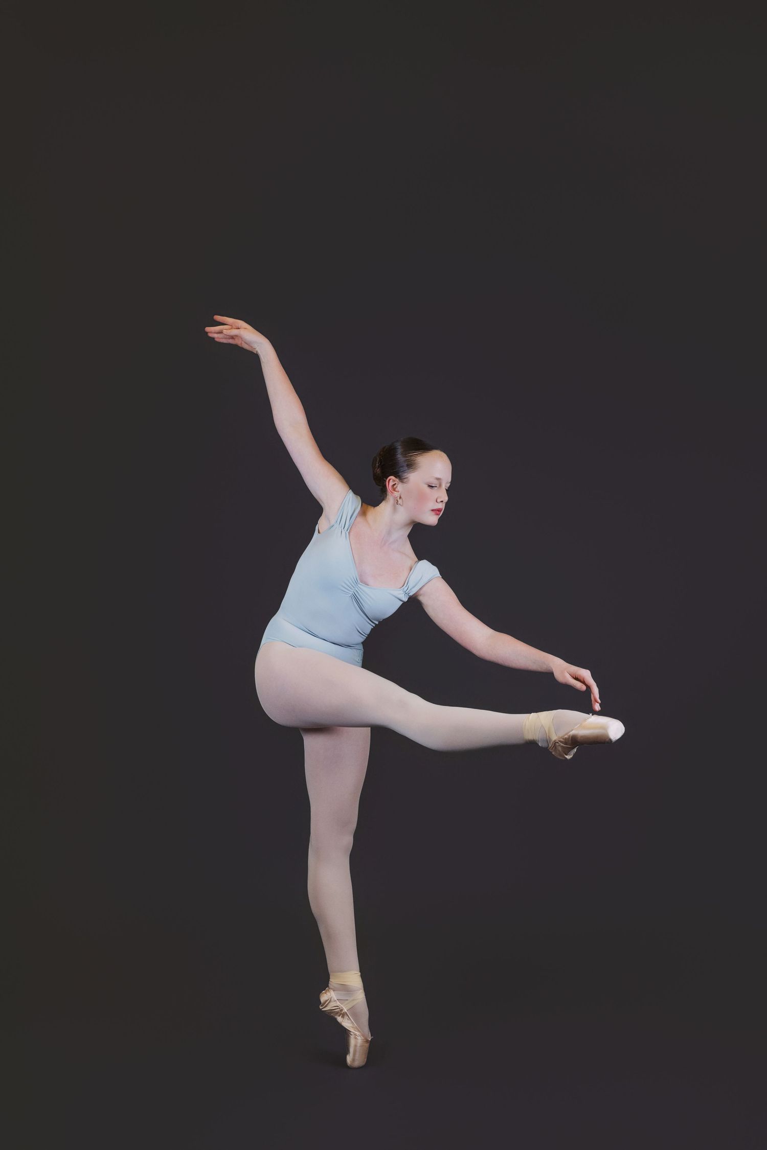 Ballet dancer in light blue leotard performs graceful arabesque poses against dark background.